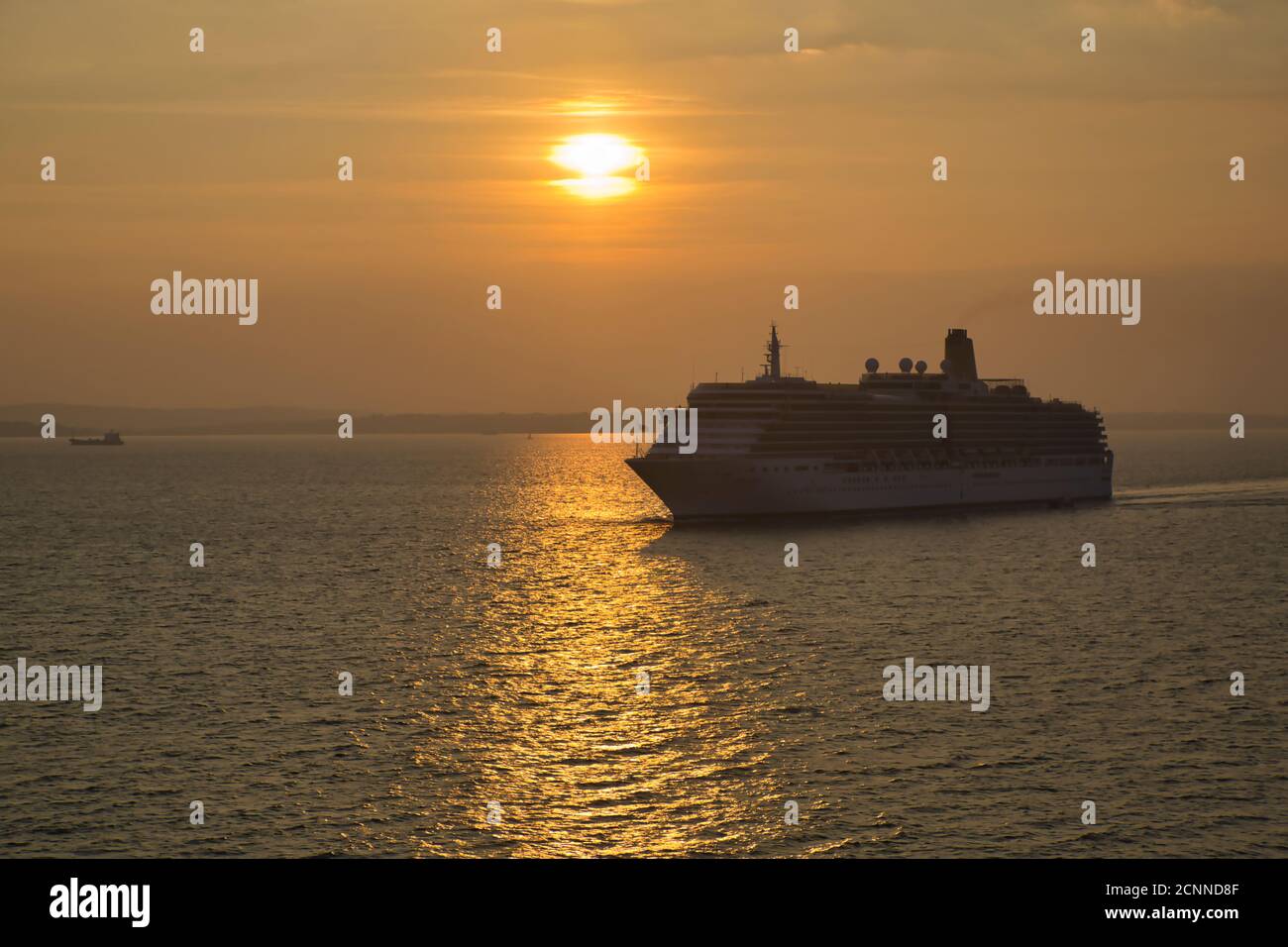 Ein Kreuzfahrtschiff, das bei Sonnenuntergang in den Hafen von Portsmouth segelt, wobei die untergehende Sonne einen Lichtweg auf der Wasseroberfläche mit dem Liner in Silhouette macht Stockfoto
