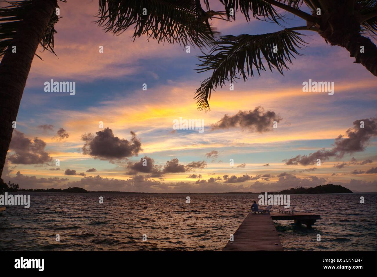 Wunderschöner tropischer Sonnenuntergang, eingerahmt von Palmen und Blättern, vor der Insel Tahiti, Französisch-Polynesien, dem Südpazifik Stockfoto