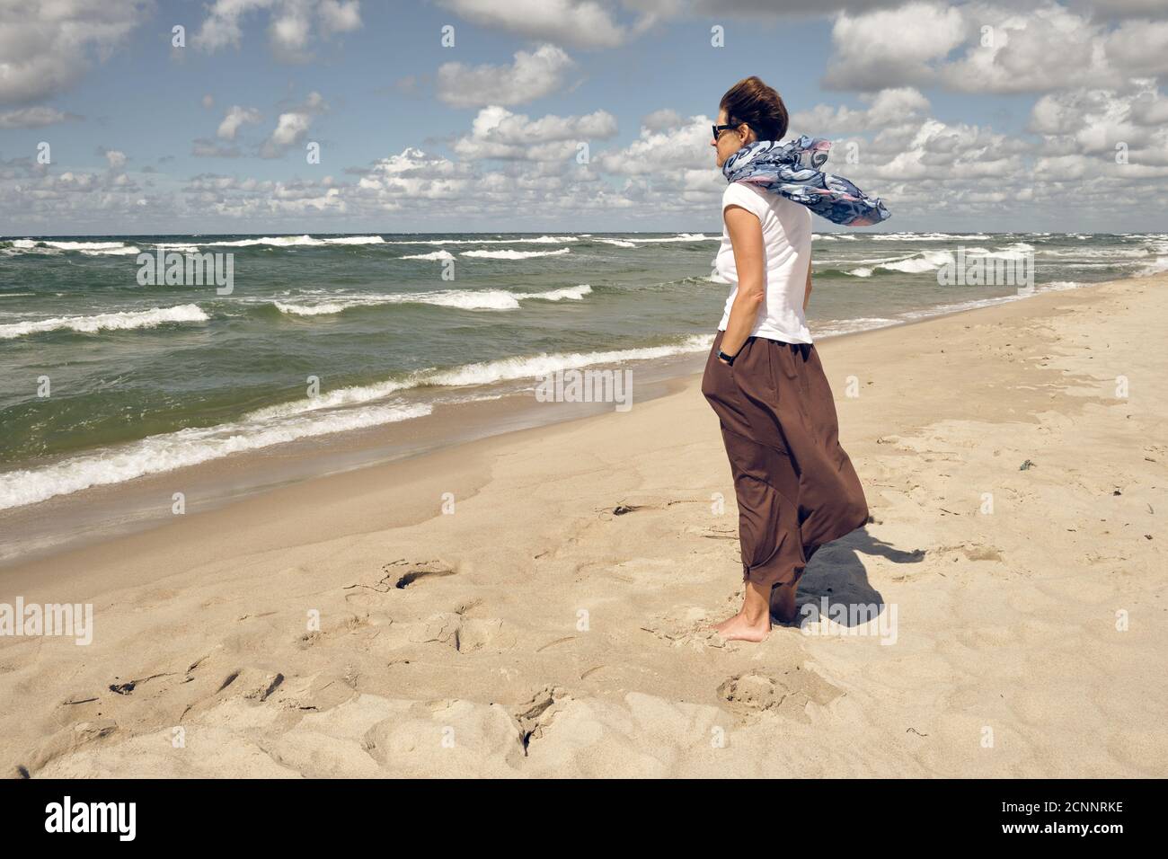 Einsame Frau mittleren Alters am Strand mit Blick auf das Meer An windigen Sommertagen Stockfoto