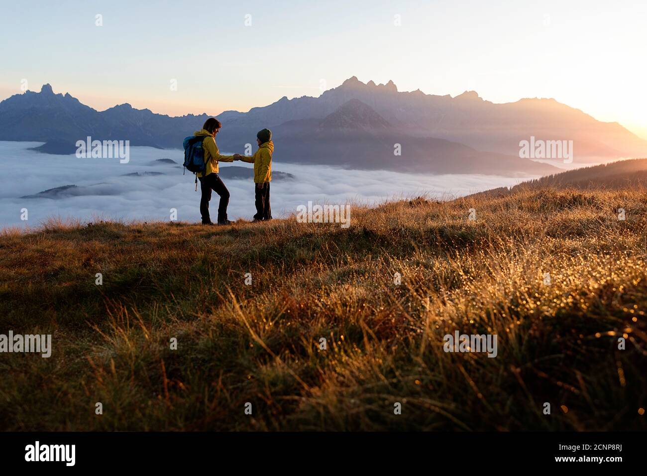 Mutter und Sohn halten Hände, während sie auf dem Rossbrand stehen Berg bei Sonnenaufgang Stockfoto