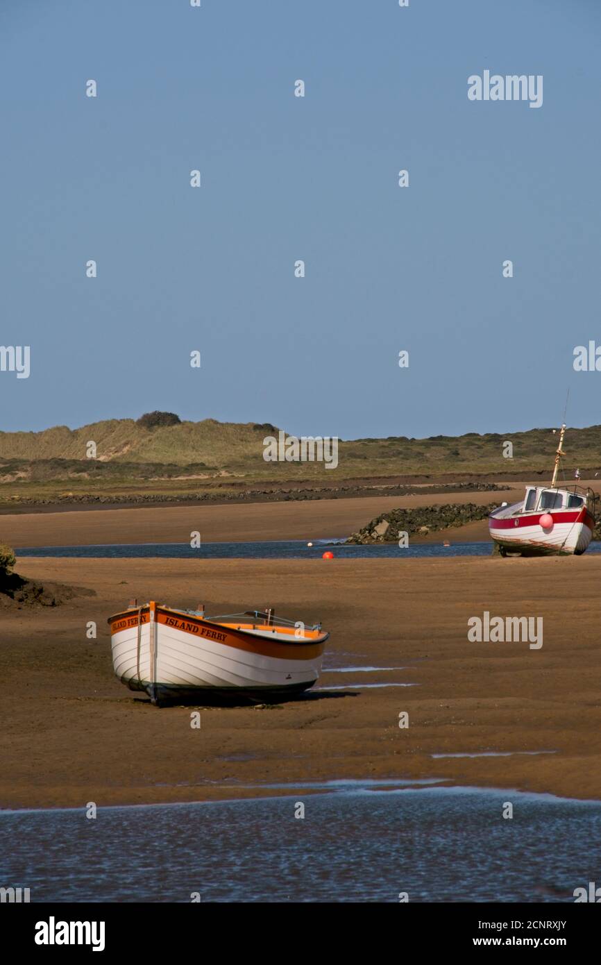 Boote festgemacht hoch und trocken bei Ebbe auf Sandbänken der Mündung. Blauer Himmel. Burnham Overy, Norfolk. Hochformat. Stockfoto