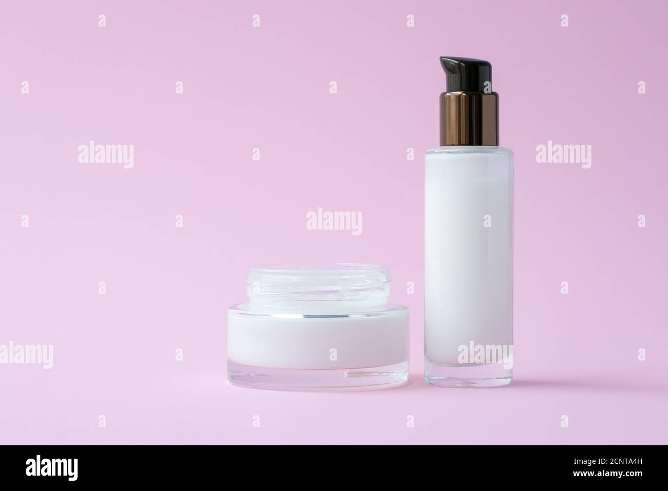 Weiße Gesichtscreme im Glas und feuchtigkeitsspendende Lotion in einer Glasflasche auf rosa Papier Hintergrund. Natürliches kosmetisches Konzept. Hautpflege und Schutz in de Stockfoto