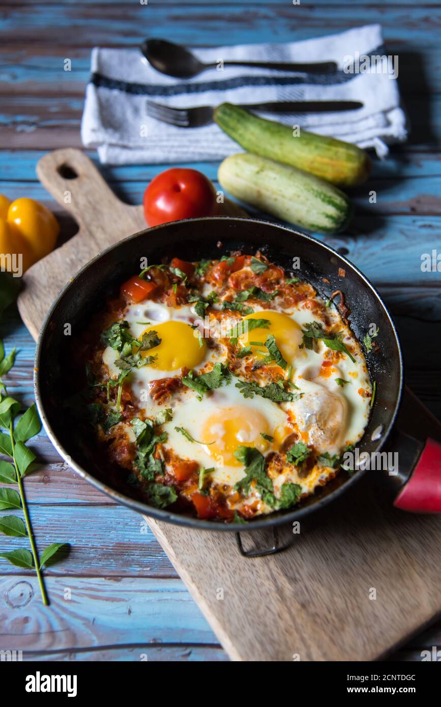 Shakshuka, ein tunesisches Gericht in einer schwarzen Pfanne zusammen mit Gewürzen auf einem Hintergrund Stockfoto