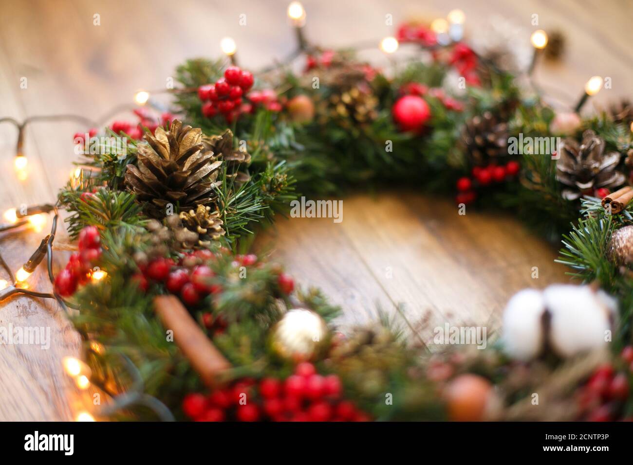 Weihnachtskranz Dekorationen schließen auf rustikalem Holz in Lichtern.  Baumwolle, rote Beeren, Ornamente und Tannenzapfen auf traditionellen  weihnachtskranz, Urlaub Stockfotografie - Alamy