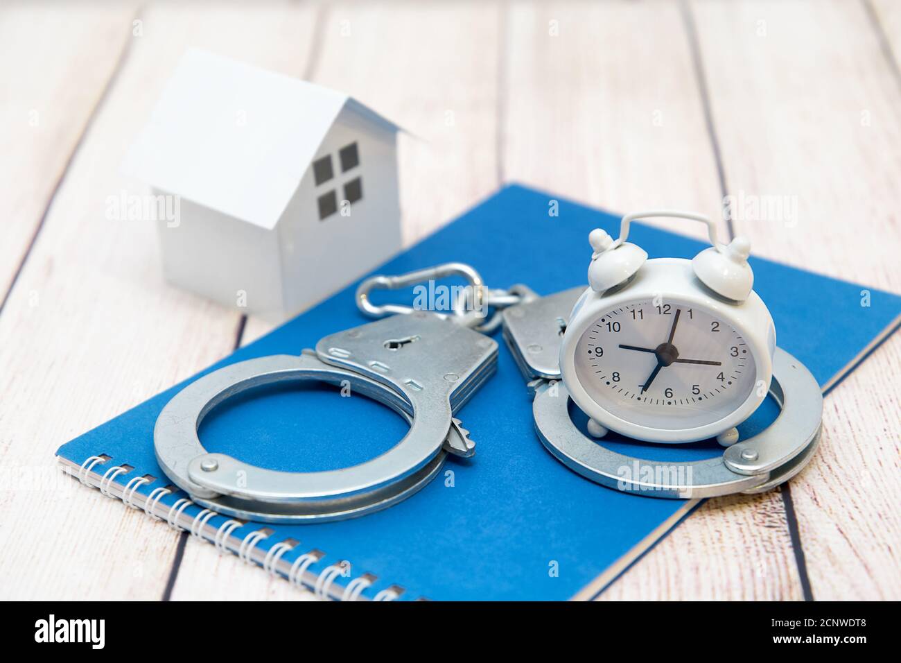 Handschellen, Uhr und ein Haus auf blauem Hintergrund. Betrug auf dem Wohnungsmarkt Stockfoto