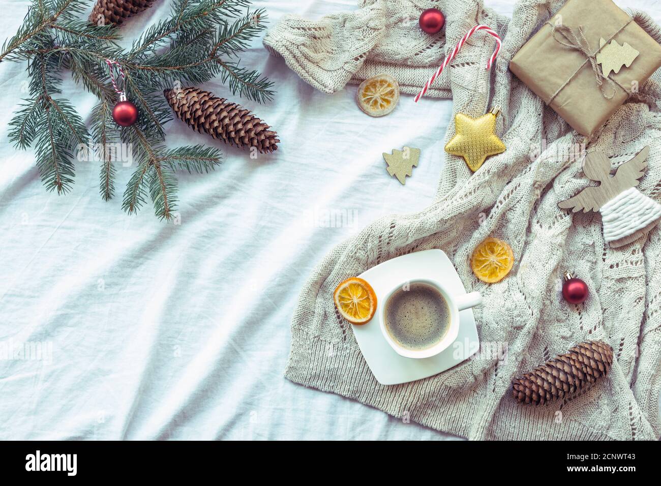 Neujahrsgestaltung mit Tasse Kaffee, Geschenkbox, Weihnachtsdekor, Tannenzweig, getrockneten Orangen und Strickpullover Stockfoto