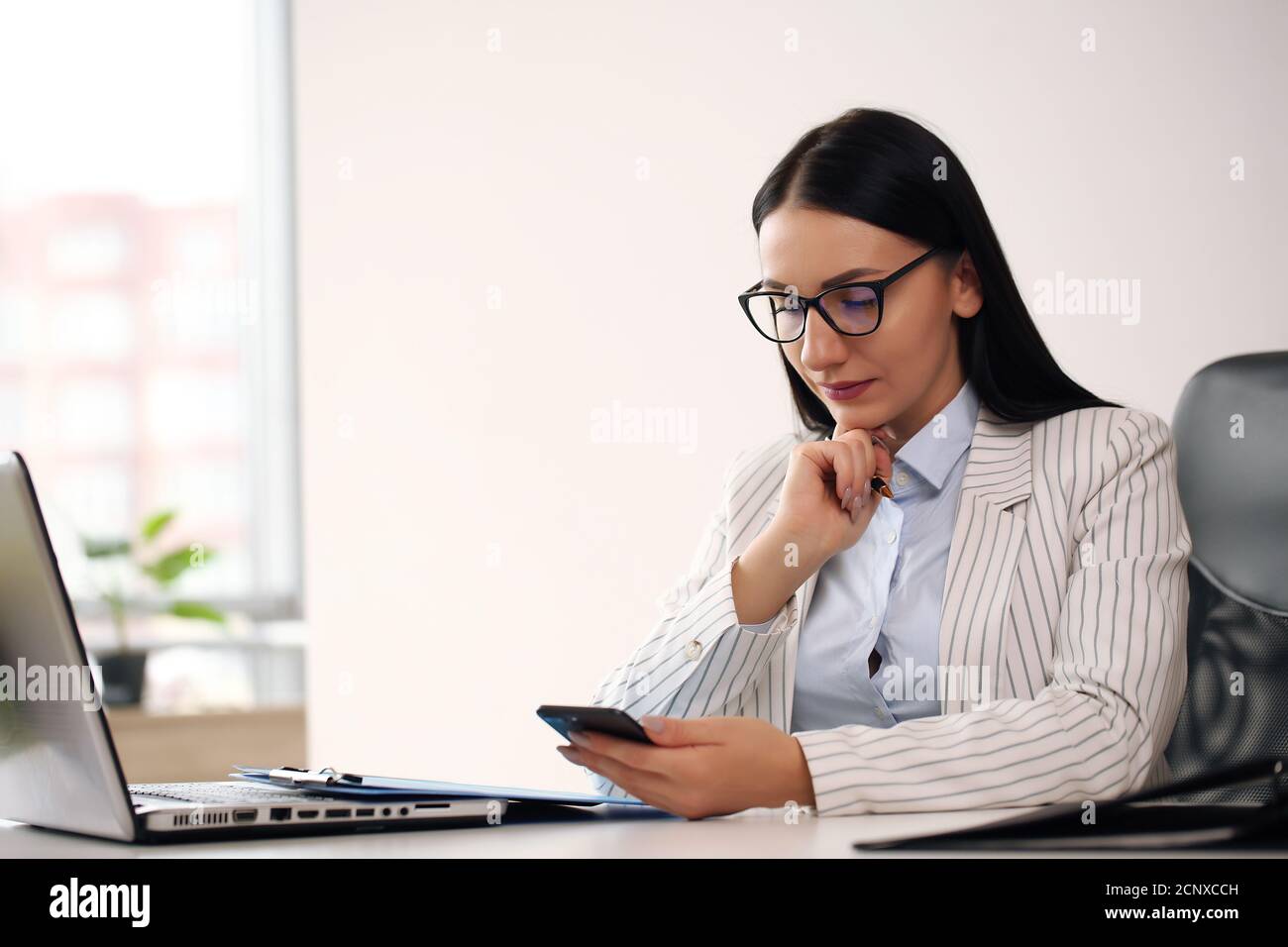 Fröhliche Brünette Dame mit wichtigen Dokument freundlich lächelnd und suchen Bei der Kamera, während Sie Ihren Laptop am Schreibtisch im Heimbüro durchsuchen Stockfoto