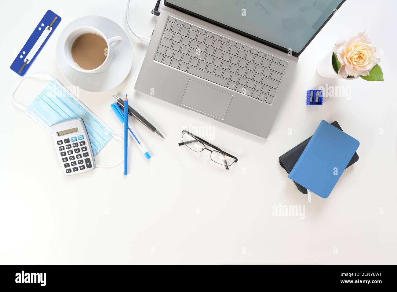 Weißer Schreibtisch mit silbernem Laptop, blauen Arbeitsmitteln und einer chirurgischen Gesichtsmaske gegen Coronavirus und Covid-19-Infektion, neues normales Geschäft Stockfoto