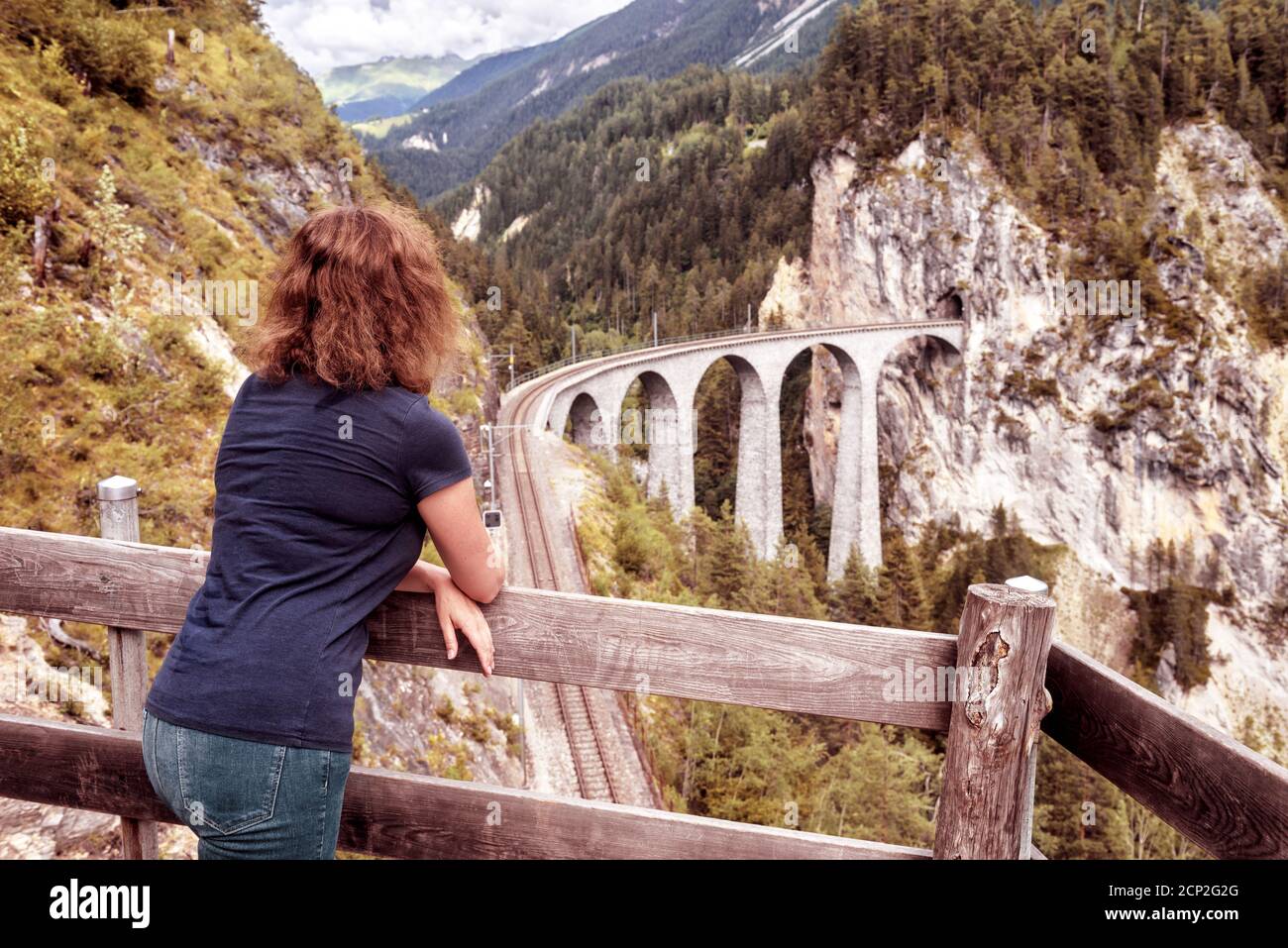 Tourist schaut auf das Landwasser Viadukt in der Schweiz. Diese Eisenbahnbrücke ist Wahrzeichen der Schweizer Alpen. Junge Frau ist auf dem Hintergrund der Berglandschaft Stockfoto