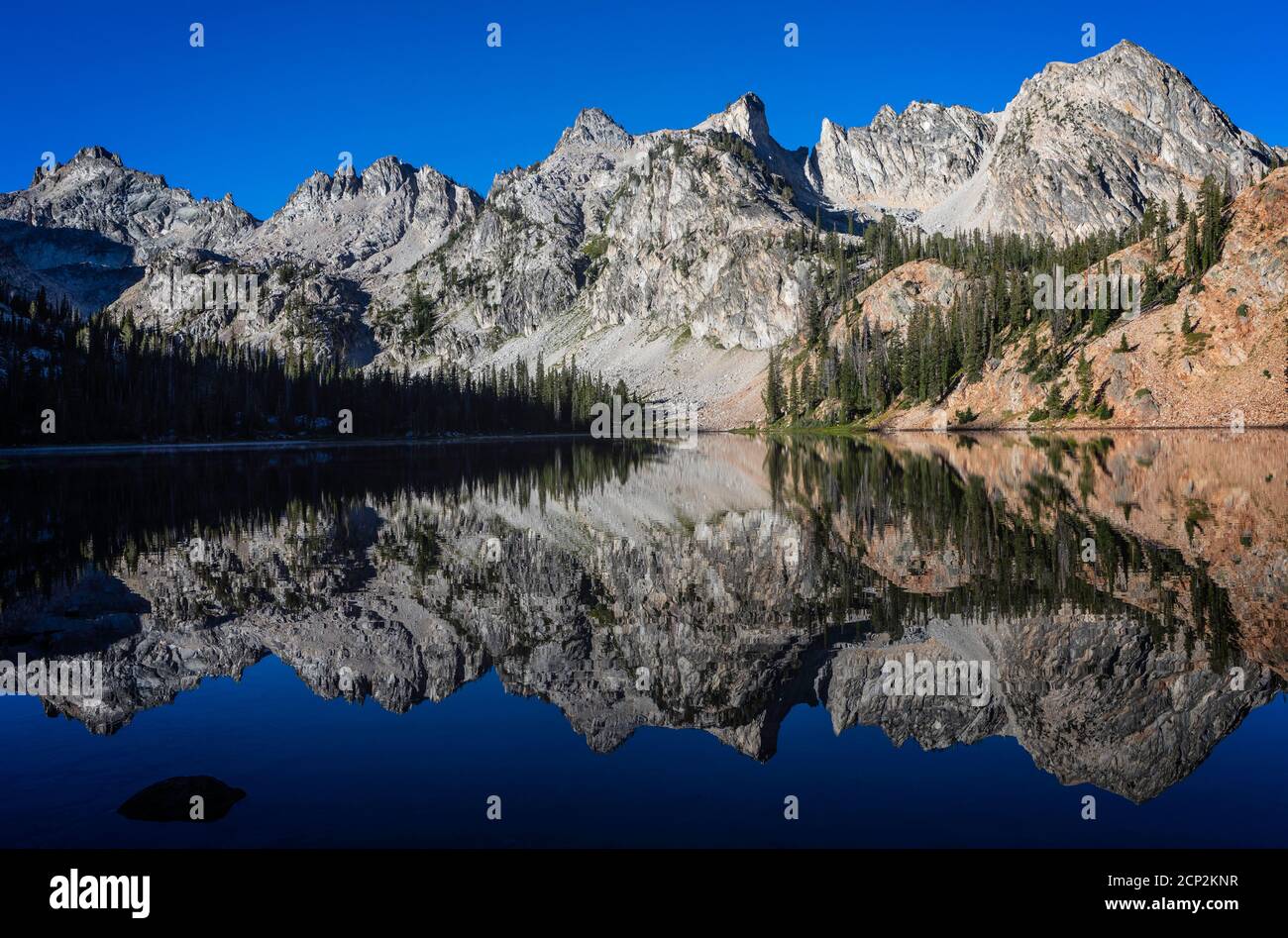 Alice Lake spiegelt die umliegenden Gipfel unter einem blauen Himmel, Sawtooth Wilderness, Idaho, USA. Stockfoto