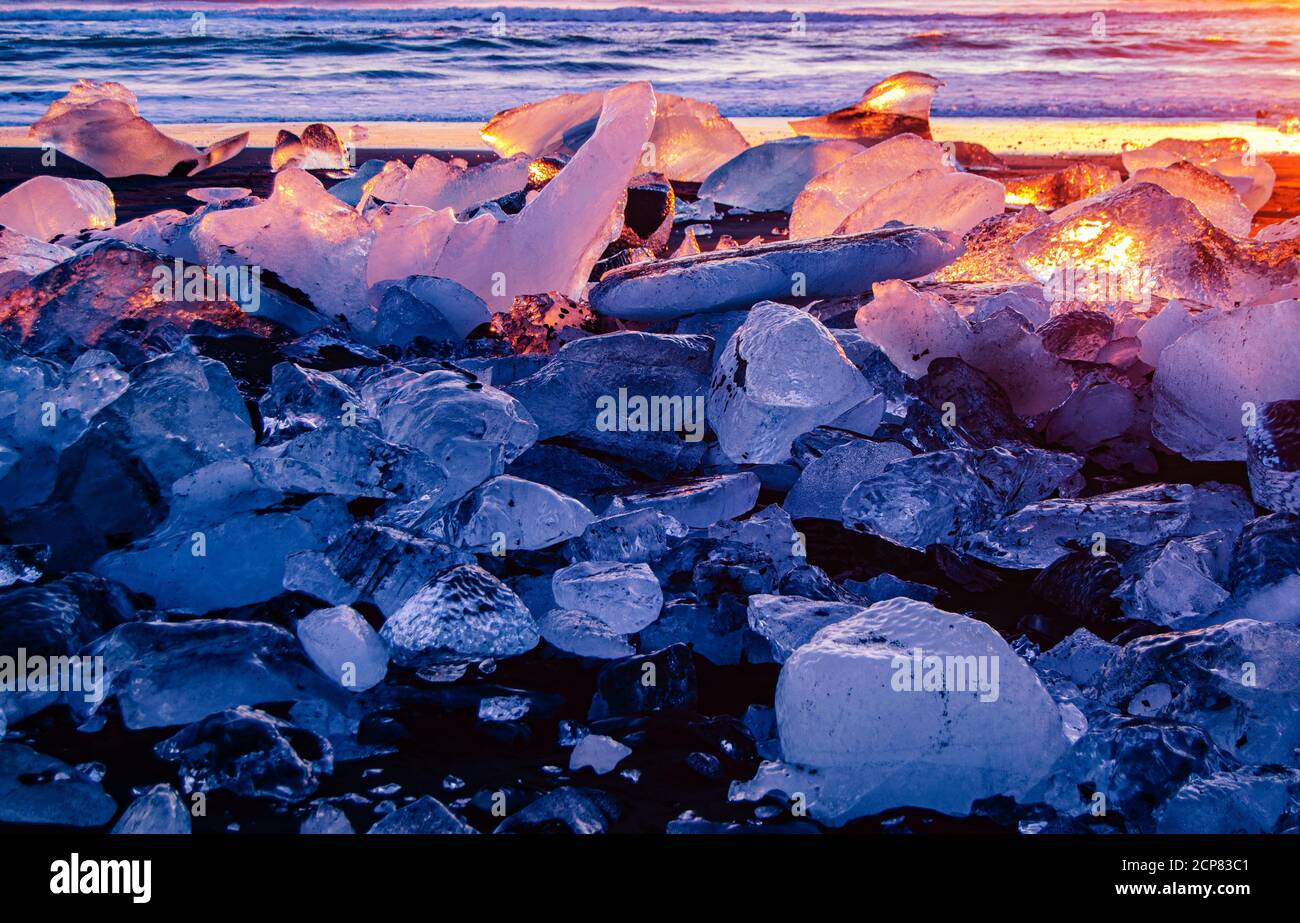 Sonnenaufgang über Diamond Beach Island, mit Licht, das in Eisbergen reflektiert wird, die von den Wellen des Ozeans geformt werden. Stockfoto