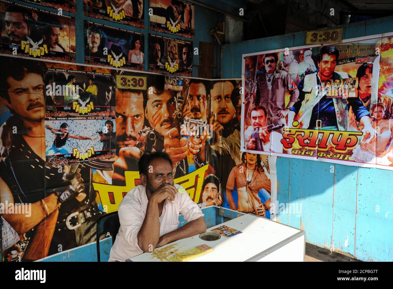 13.12.2011, Mumbai (Bombay), Maharashtra, Indien, Asien - EIN Mann sitzt an der Kasse eines kleinen Kinos mit bunten Filmplakaten geschmückt. Stockfoto