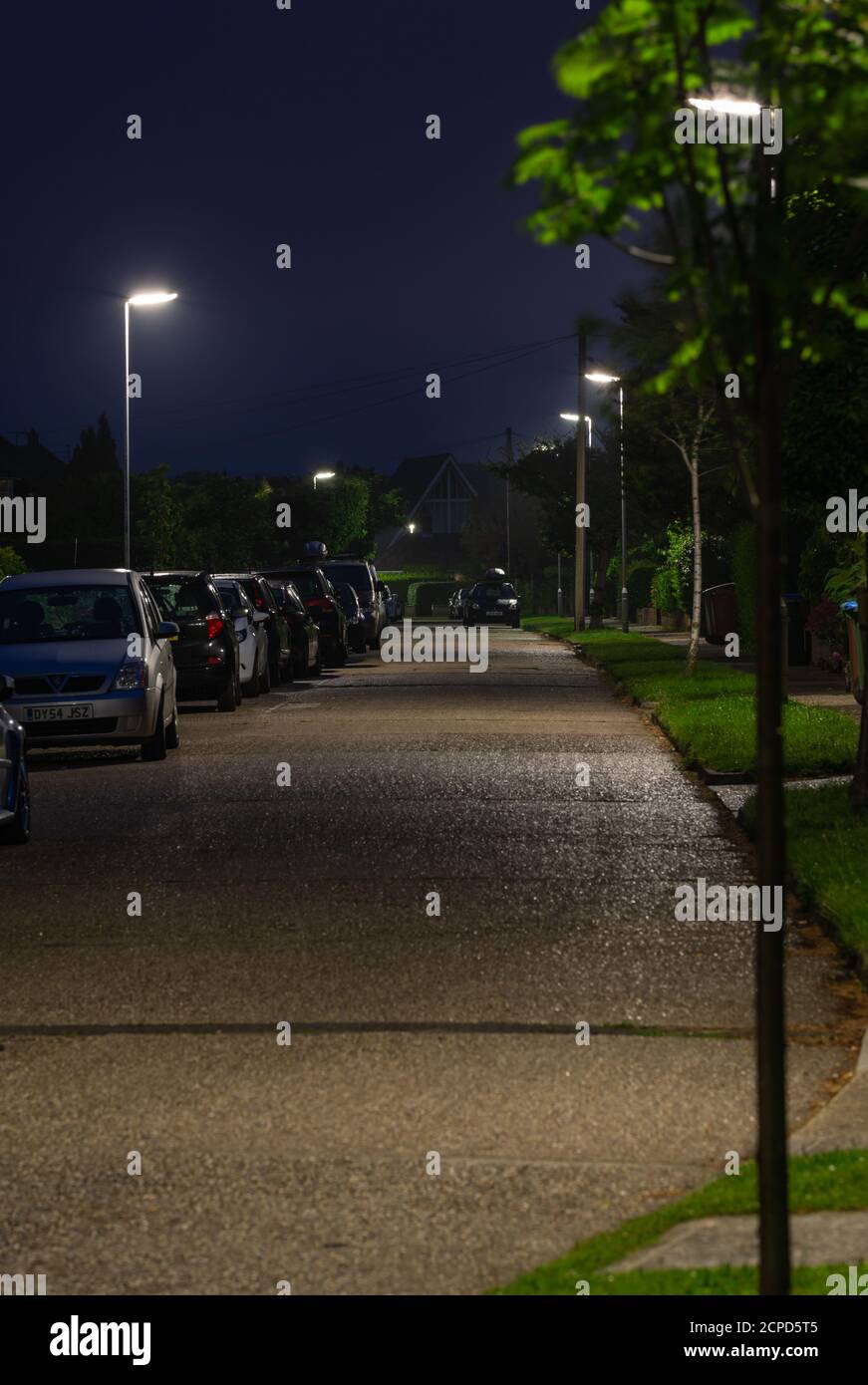 Straßenlaternen auf einer Straße, auf der die Laternenpfosten in einer ruhigen Wohnstraße in West Sussex, England, Großbritannien, eingeschaltet sind. Stockfoto