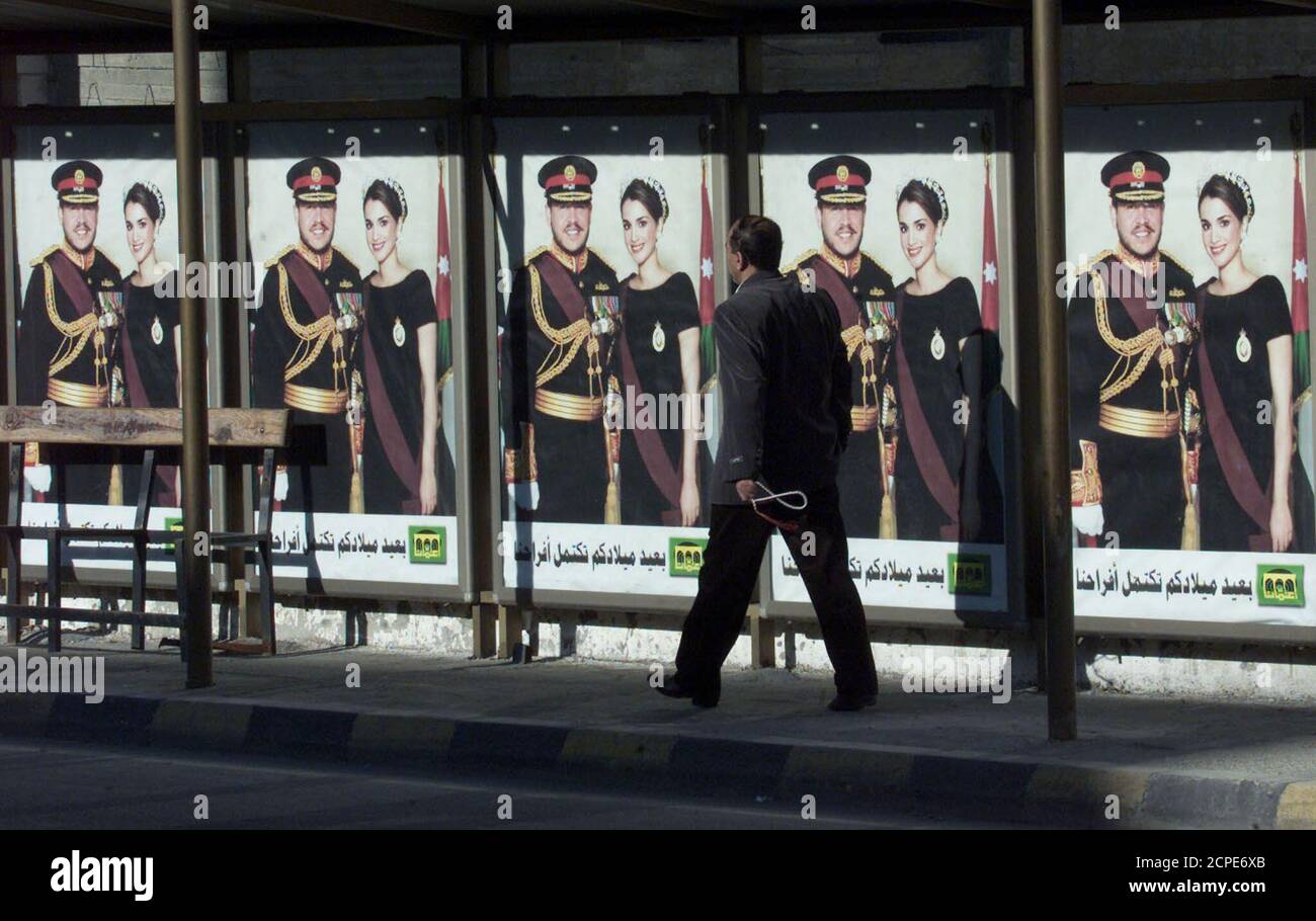 Ein Polizist passiert Plakate von Jordaniens König Abdullah und seiner Frau Königin Rania in einer Hauptstraße in Amman 30. Januar 2002. König Abdullah, einer der jüngsten arabischen Staatsoberhäupter, wurde am Mittwoch 40 Jahre alt, aber die Feierlichkeiten anlässlich seines Geburtstages waren in einem Land, das tief über die Verschärfung der Gewalt im Nahen Osten besorgt war, äußerst unaufgeblich. REUTERS/Ali Jarekji AJ/WS Stockfoto