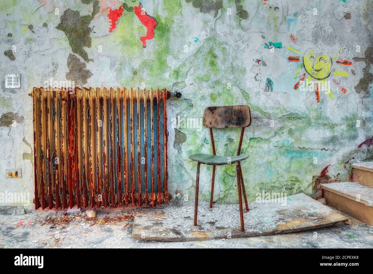 Ein kleiner Stuhl in einem alten verlassenen Gebäude, Schutt und Staub, alter rostiger Heizkörper und Kinderzeichnungen an der abblätternden Wand Stockfoto