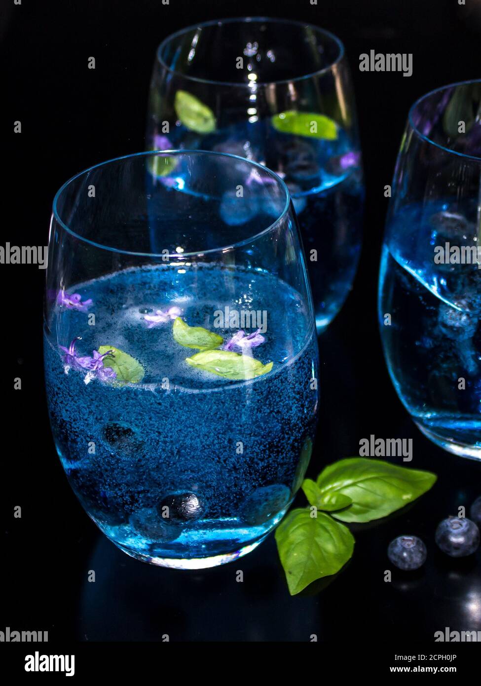 Drei Gläser hellblau, Gin und Tonic, mit Heidelbeer aromatisiertem Tonic, garniert mit frischen Heidelbeeren, Basilikumblättern und Rosmarinblüten Stockfoto