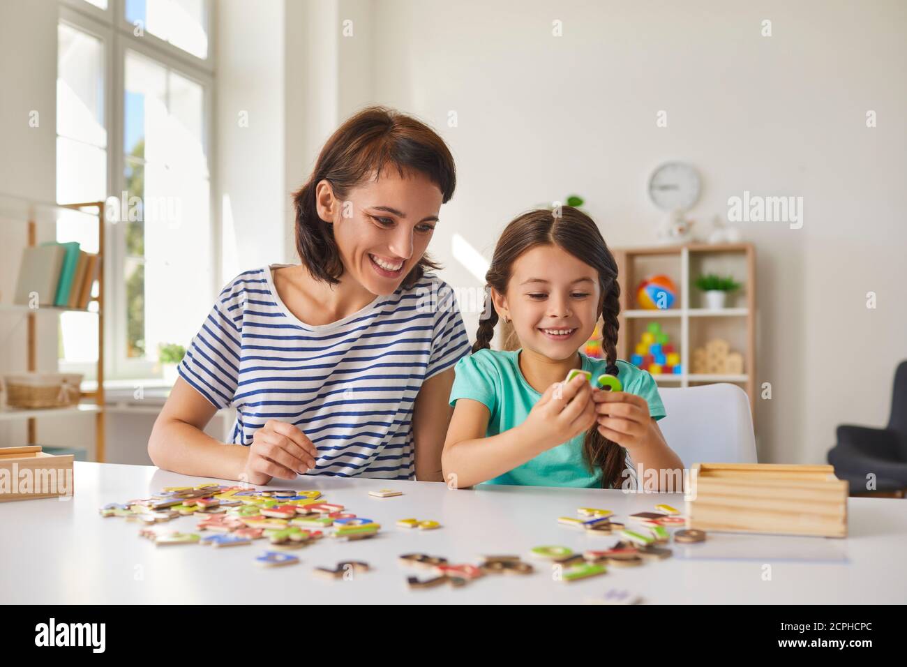 Mama und kleine Tochter zusammen Puzzles während sitzen an einem Tisch im Zimmer. Stockfoto