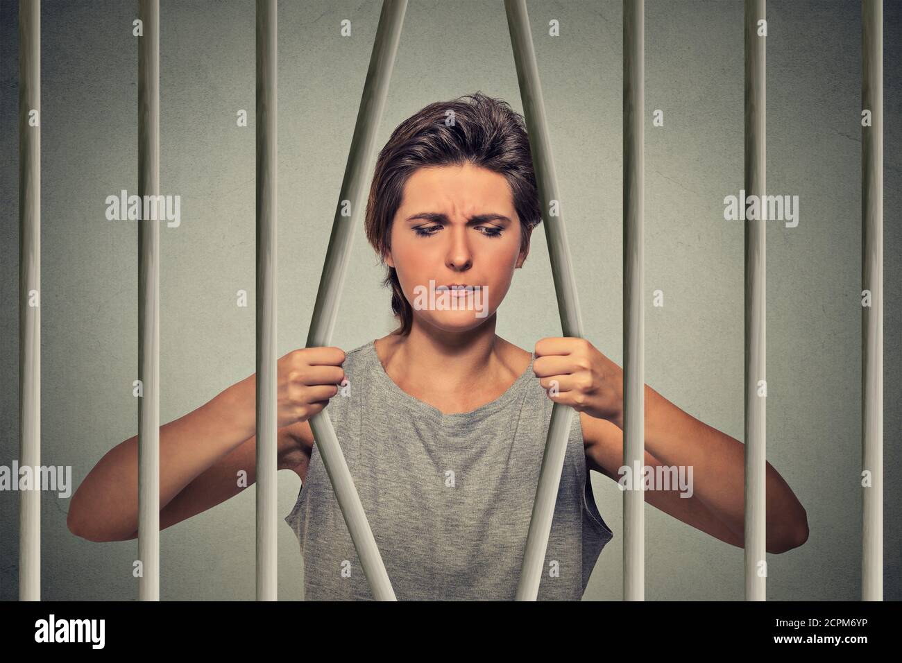 Gestresste verzweifelte traurige Frau, die ihre Gefängniszelle auf grauem Wandhintergrund verbiegt. Lebensbeschränkungen, Gesetzesverletzung Konsequenzen Konzept. F Stockfoto