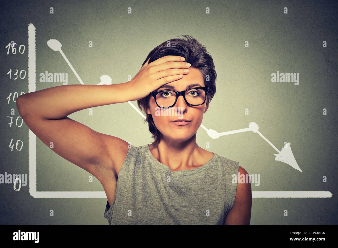 Gestresst schockiert Frau in Brille mit Finanzmarkt Chart Grafik geht nach unten auf grauen Bürowand Hintergrund. Schlechtes Economy-Konzept. Gesichtsausdruck Stockfoto