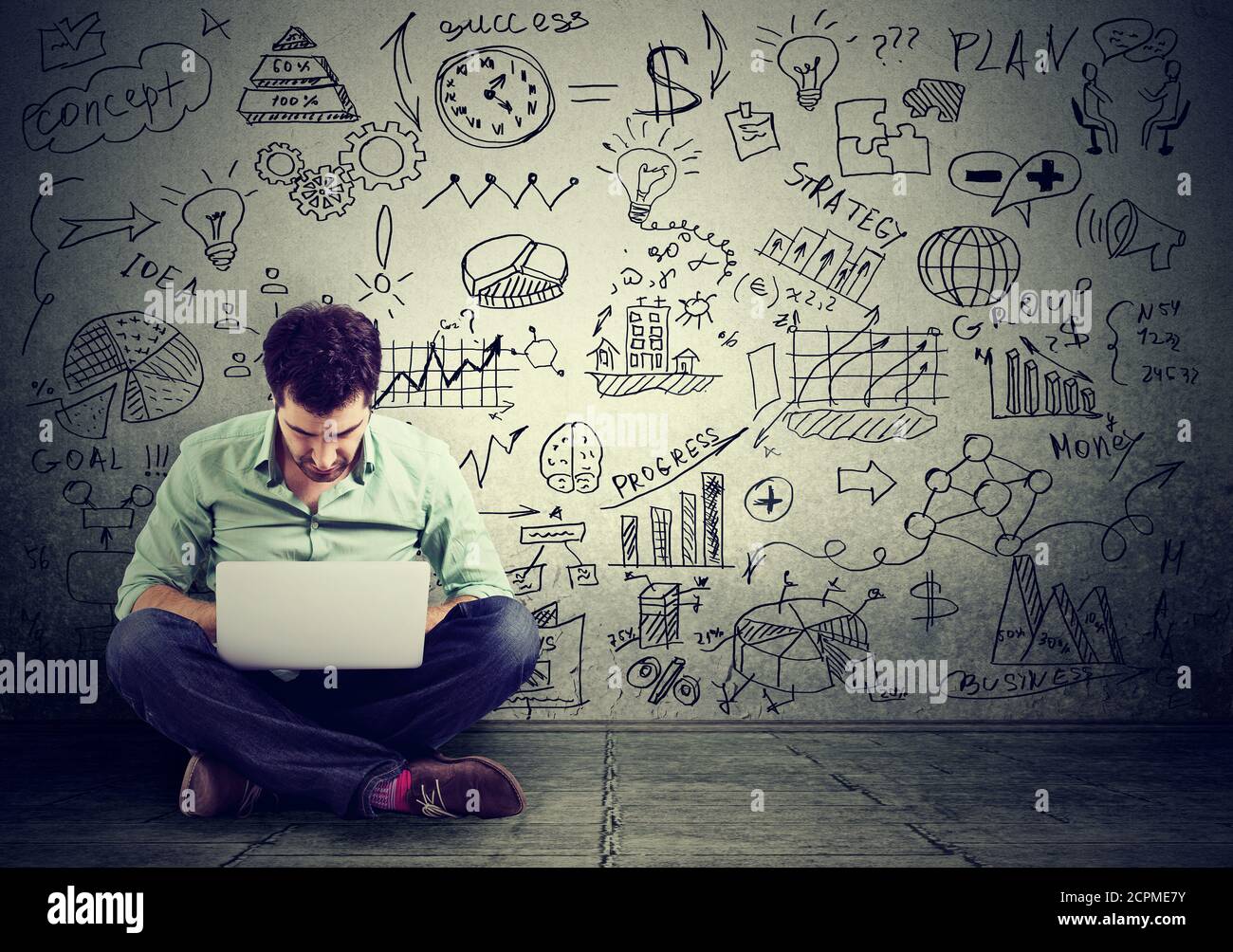 Junger Mann, der am Computer arbeitet, sitzt auf einer Etage und lernt Online-Zeichnung Schemen Business-Plan an der Wand Stockfoto