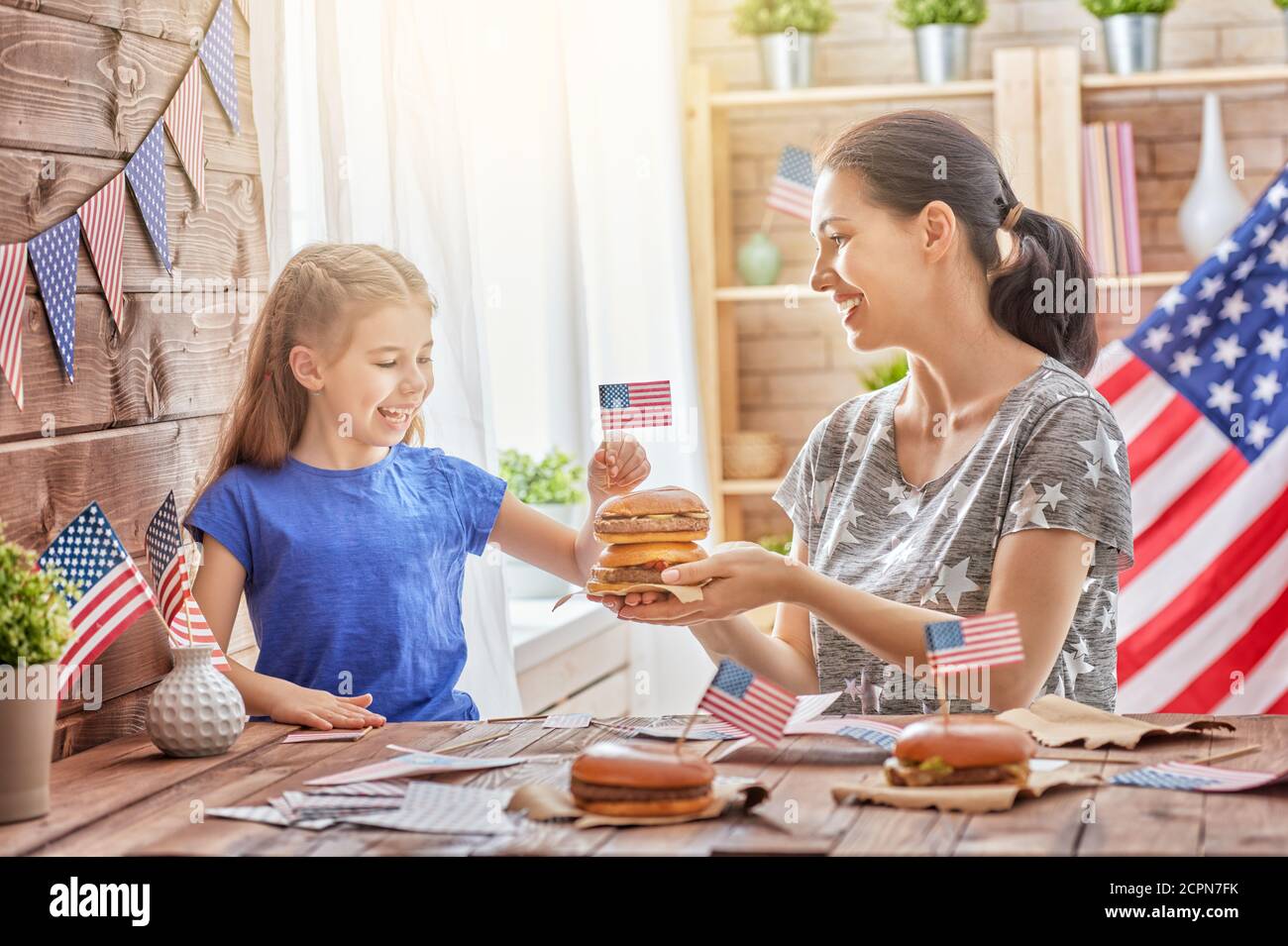 Patriotischer Urlaub. Mutter und Tochter machen Burger. Glückliche Familie feiern 4. Juli. Nettes kleines Kind Mädchen und ihre Mutter mit amerikanischen Fla Stockfoto