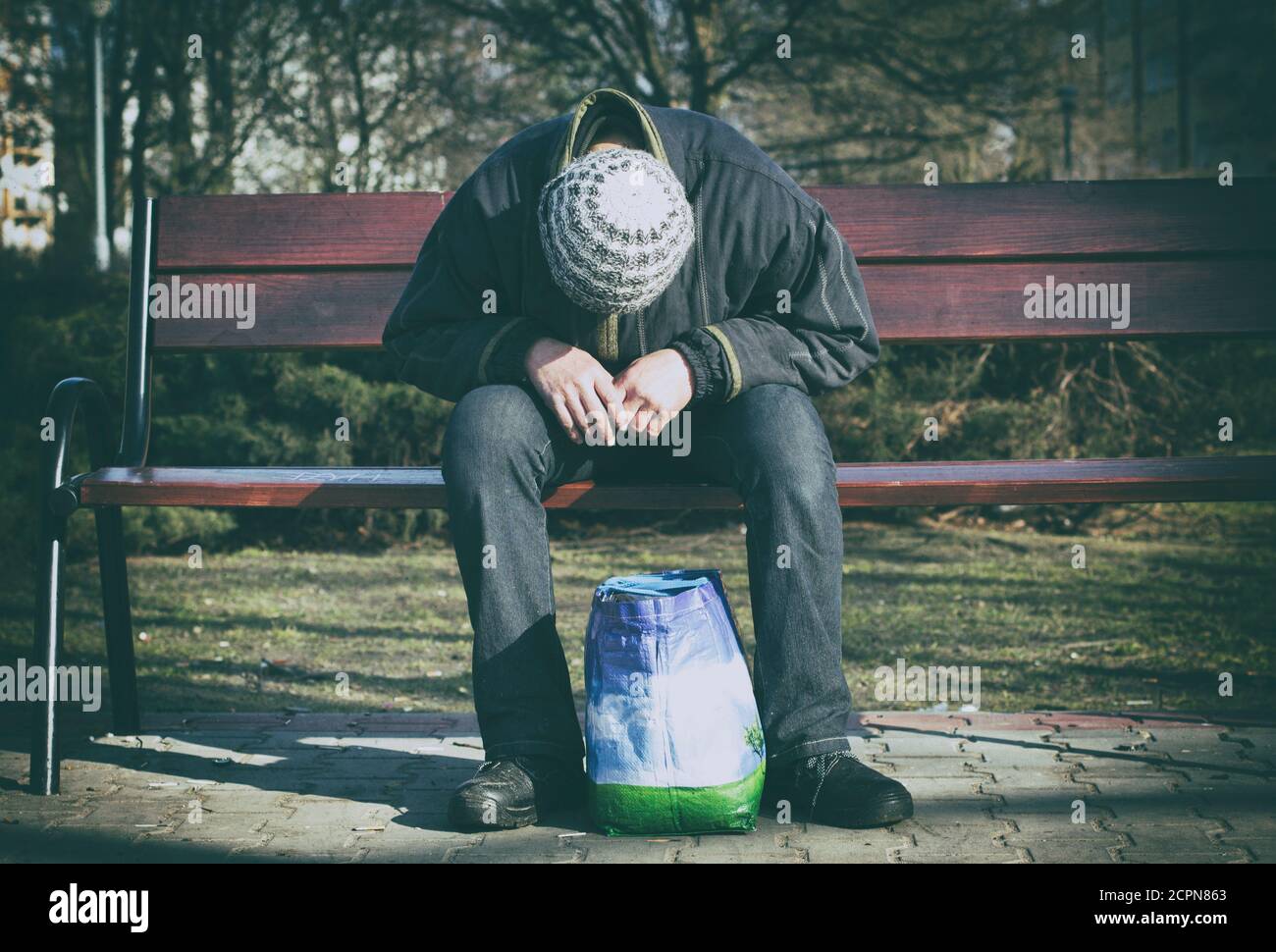 Deprimiert und hoffnungslos - ein Mann, der allein nach Drogen und Alkohol auf einer Holzbank sitzt. Stockfoto