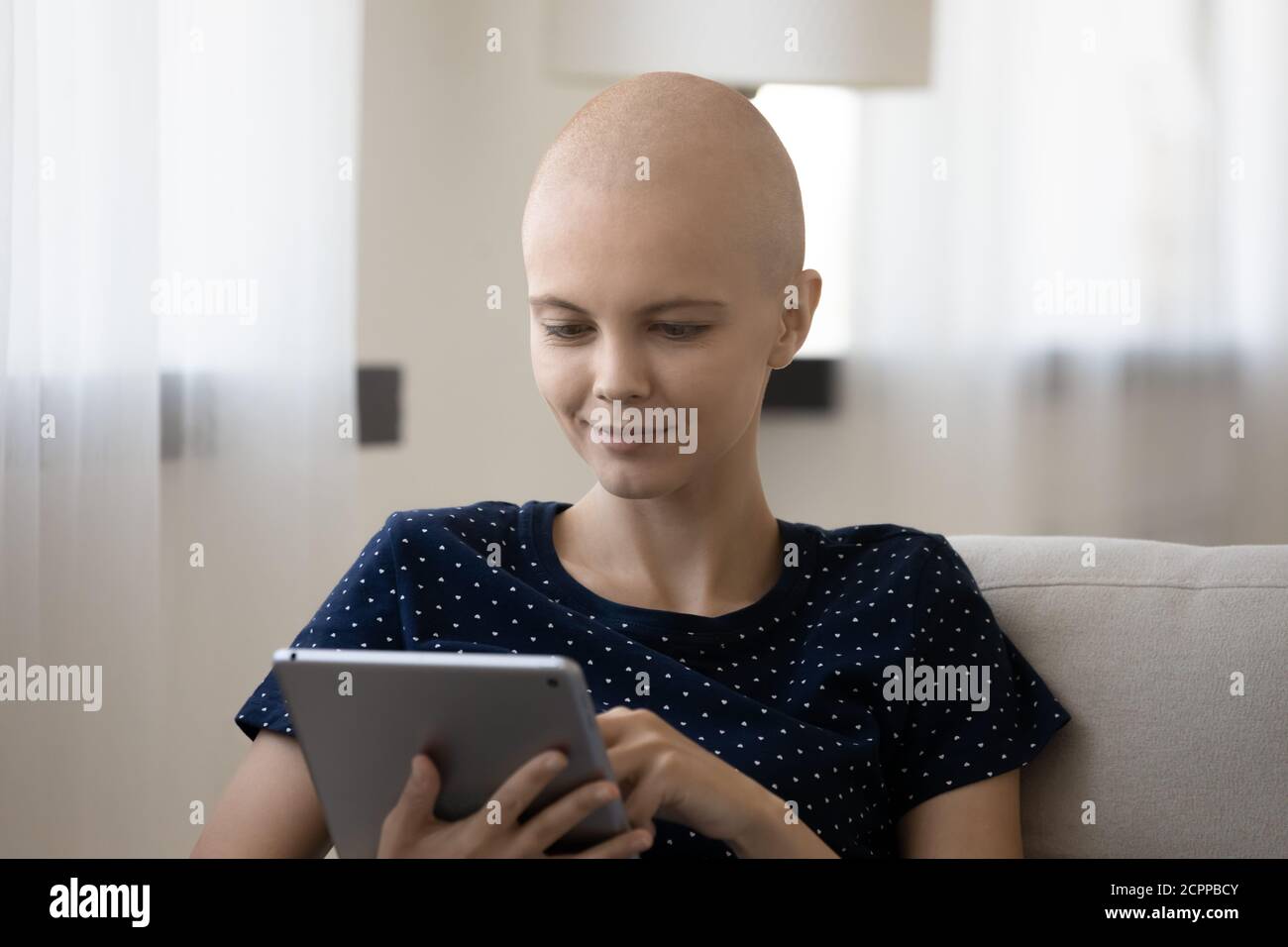 Positive kranke haarlose Frau entspannen zu Hause mit Tablet Stockfoto