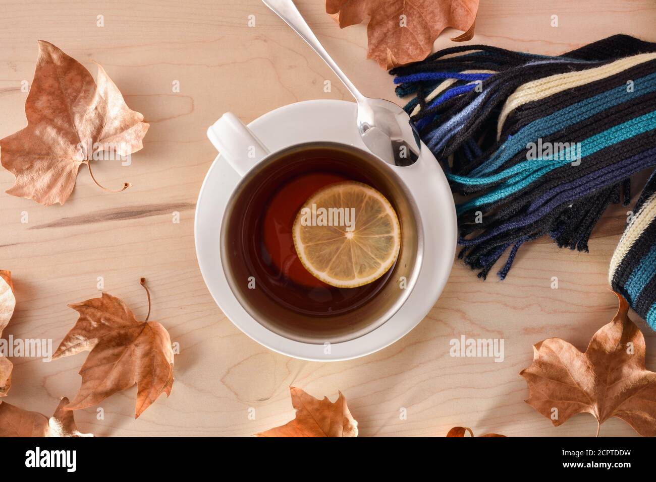 Herbstliches Konzept mit Detail einer Tasse mit rotem Tee mit Zitrone auf einem Schal auf einem Holztisch mit trockenen Blättern auf der Oberseite. Draufsicht Stockfoto