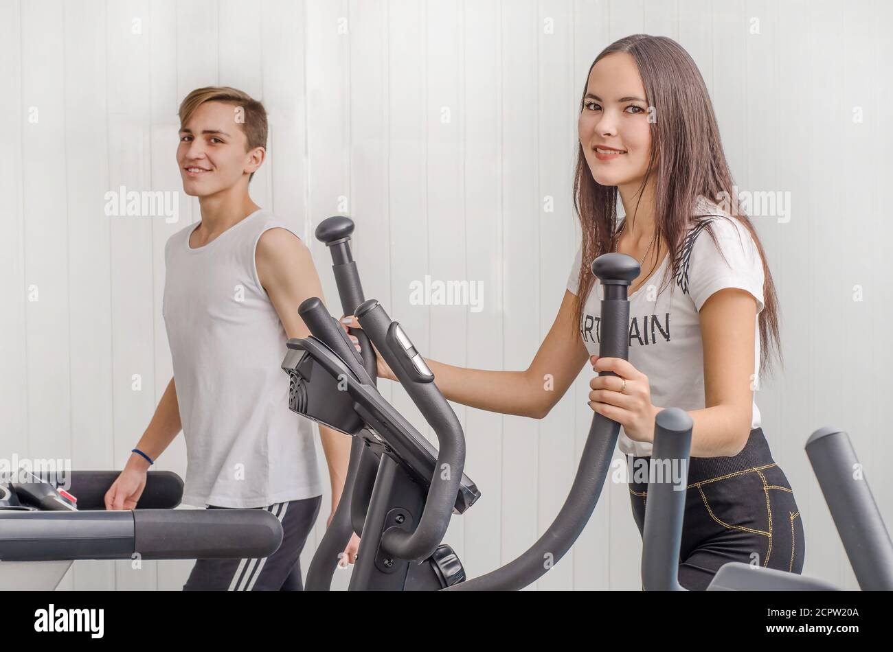 Ein Mädchen und ein Mann im Fitnessstudio trainieren auf Herz-Kreislauf-Geräten. Stockfoto