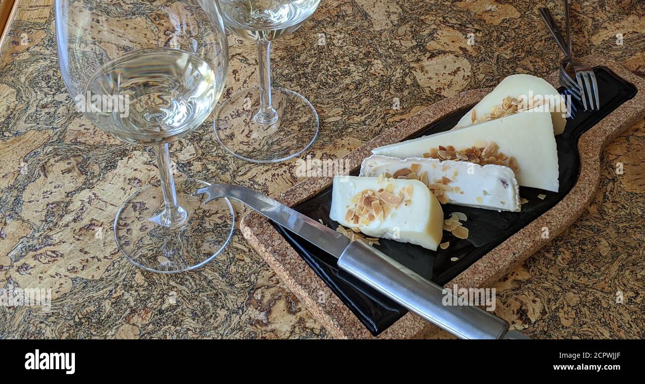 Käseplatte Nahaufnahme. Holz- und Marmorplatte mit verschiedenen Käsesorten und Mandeln neben einem Weinglas auf einem Holztisch. Stockfoto