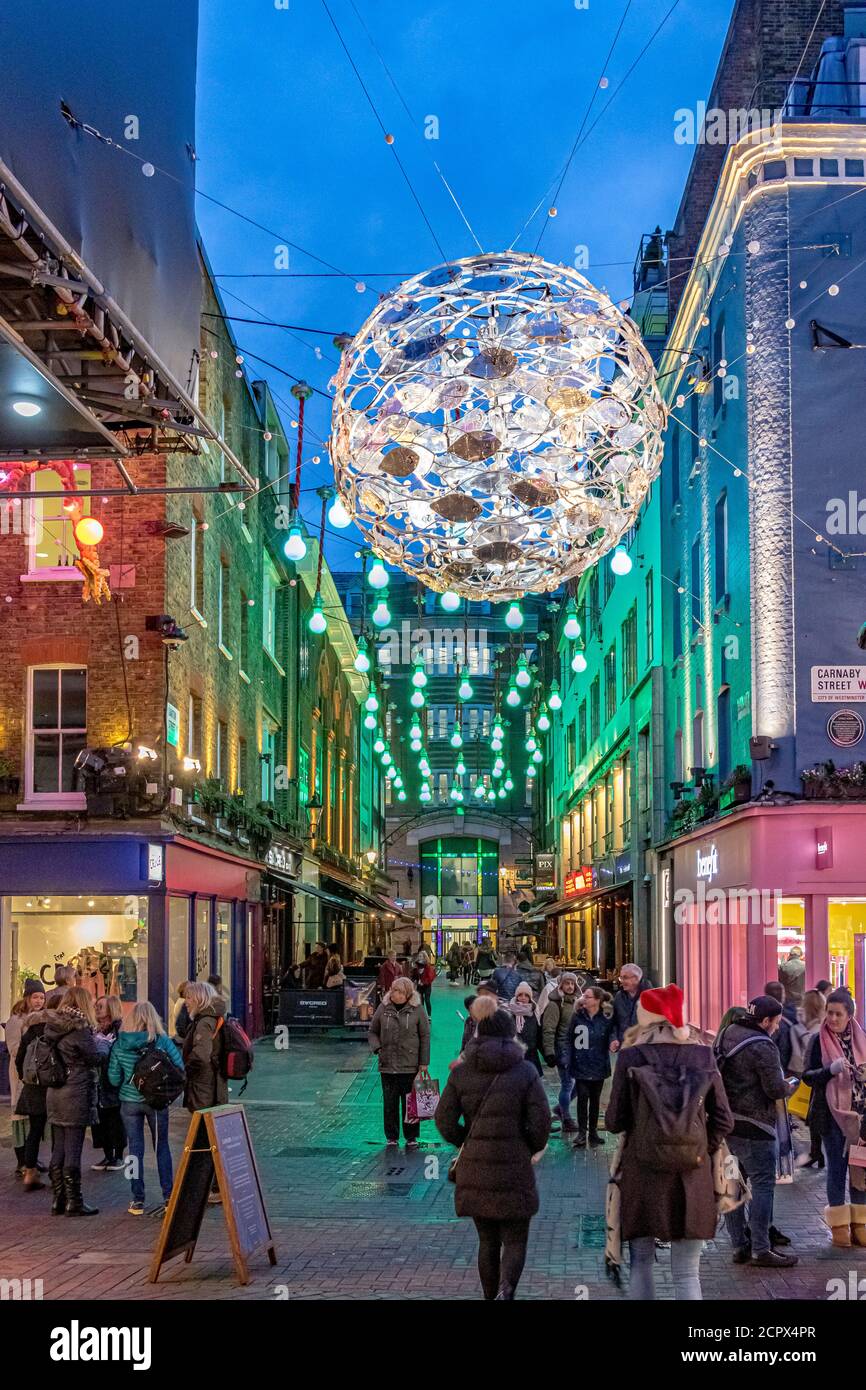 Menschenmassen, die zu Weihnachten entlang der Carnaby Street mit dem Ocean-Motto Carnaby Project Zero Christmas Lights Overhead, London, Großbritannien, spazieren Stockfoto