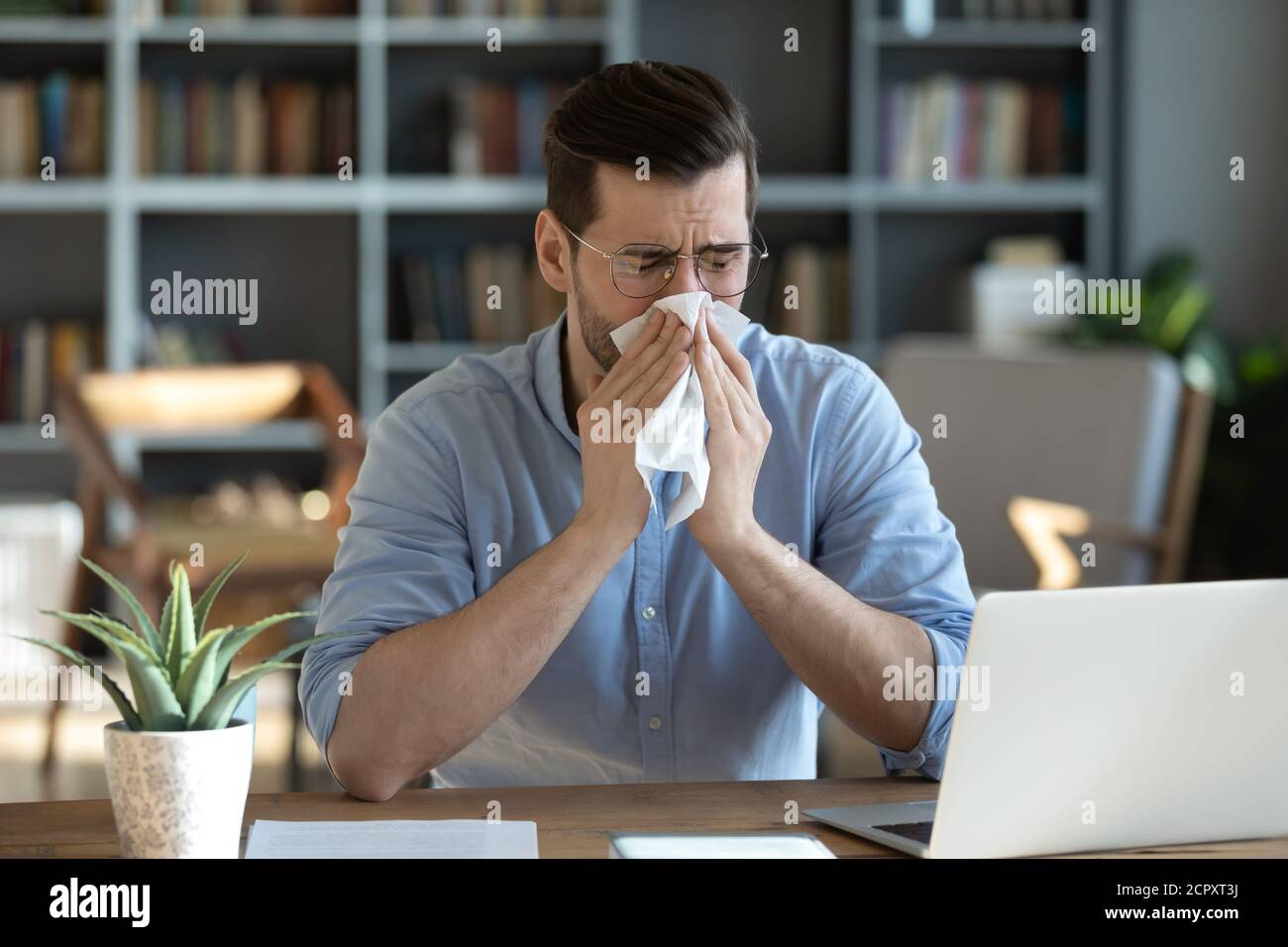 Kranker Mann blasen Nase arbeiten zu Hause am Arbeitsplatz Stockfoto