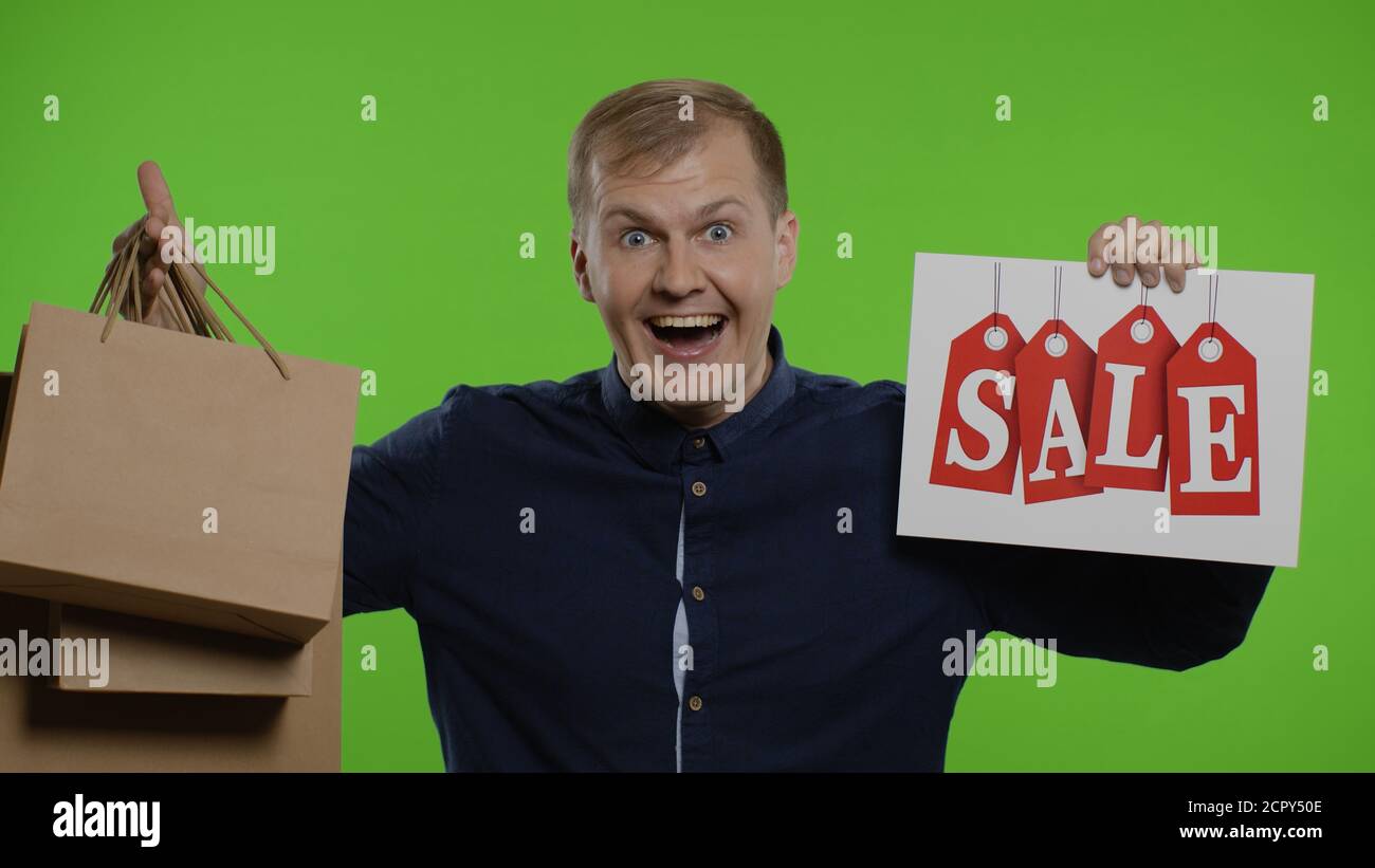 Schockiert erstaunt Emotionen des Store man Client. Überrascht Kerl zeigt Einkaufstaschen und Verkauf Wort, Blick erstaunt durch niedrige Kosten Kauf, Rabatt. Innenaufnahme auf Chroma-Key-Hintergrund. 6k Downscale Stockfoto