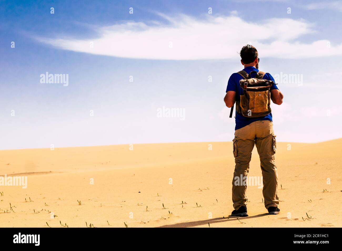 Outdoor Wüste Abenteuer und alternative Tourismus und touristische Aktivität mit Mann von hinten stehend mit Rucksack suchen eine Sandwüste Dünen und blau s Stockfoto