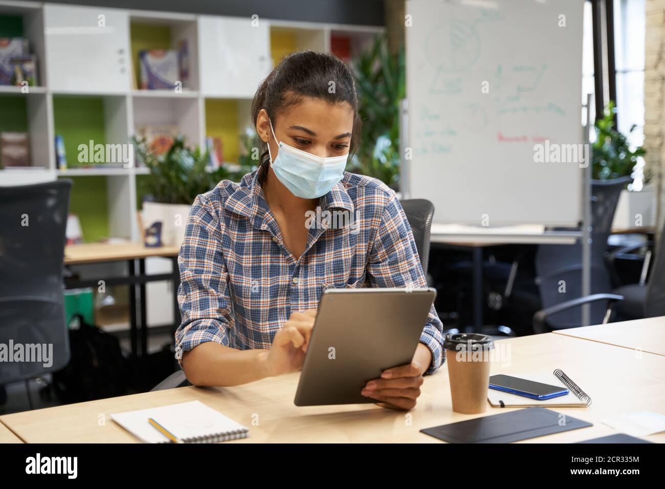 Zurück ins Büro. Junge Frau, weibliche Büroangestellte trägt eine schützende Gesichtsmaske mit einem digitalen Tablet, während sie im Büro sitzt. Geschäft und Arbeit während und covid 19 Ausbruch, soziale Distanzierung Stockfoto