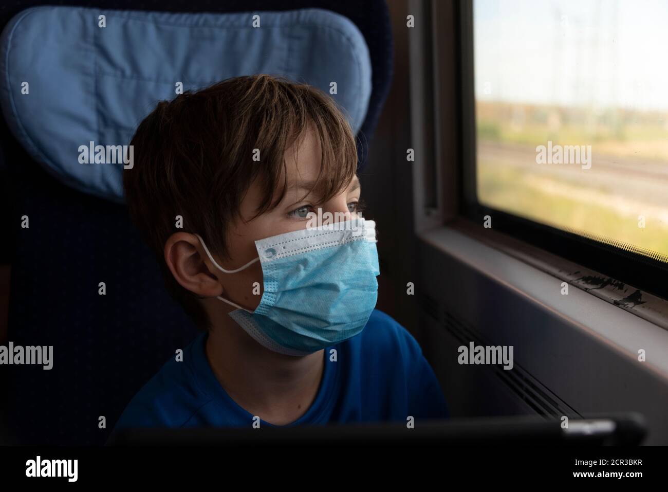 Boy sitzt in einem Zug mit Maske, Atemschutzmaske, medizinischer Maske, Mund- und Nasenschutz Stockfoto