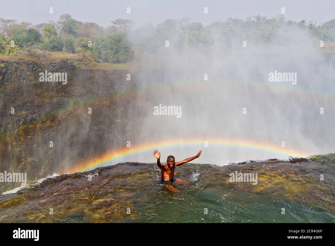 Guide am Lip of Devil's Pool an den Victoria Falls. Es sieht so aus, als ob er über den Wasserfall hinweggefegt wird, aber eine dicke Felsenlippe schützt die Menschen. Victoria Falls ist fast eine Meile breit und 360 Fuß tief und aus der Luft, sieht aus wie die Erde in zwei gerissen wurde. Sambia, Afrika. Stockfoto