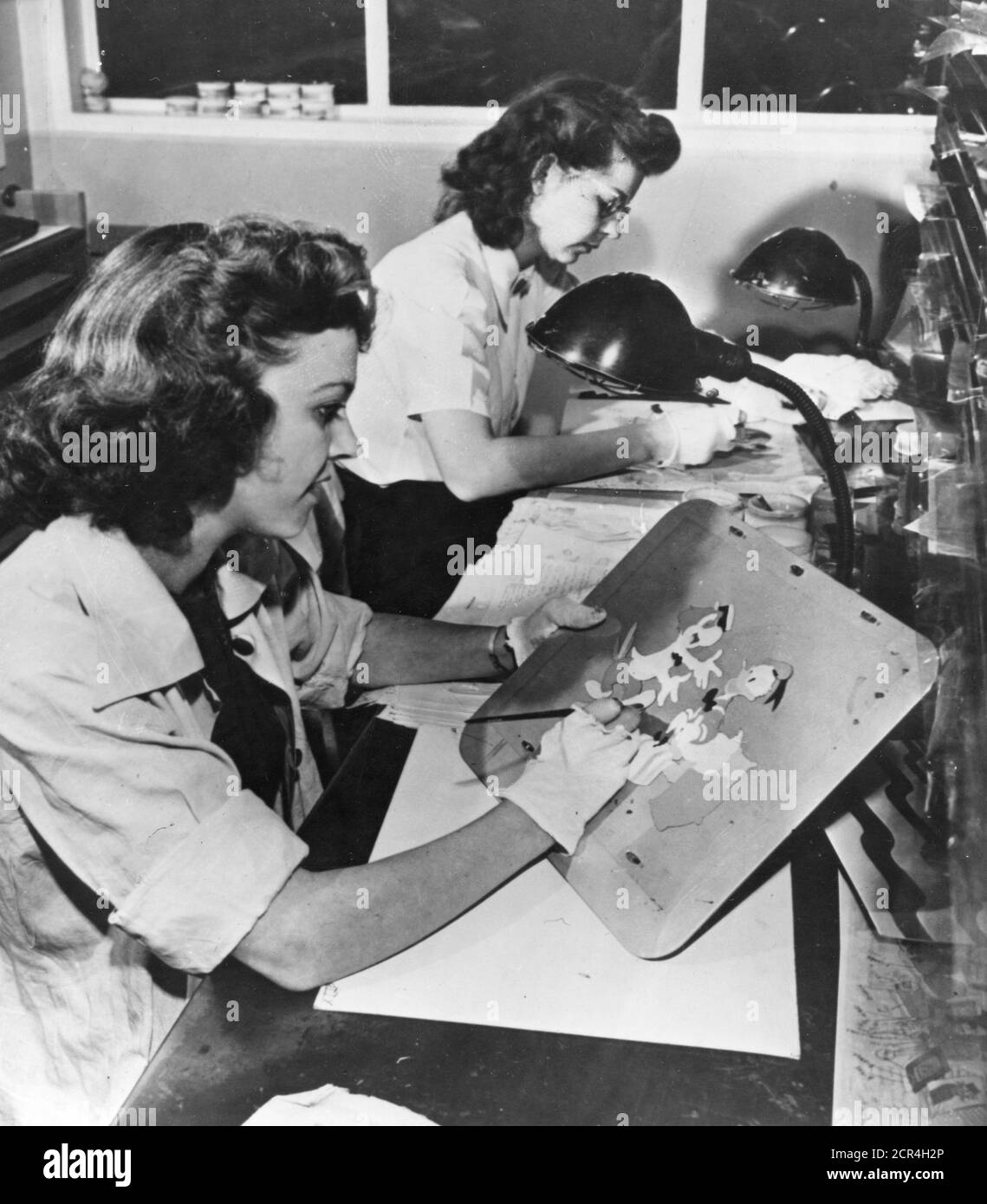 Während des Animationsprozesses, wenn eine Reihe von Animationszeichnungen fertiggestellt ist, gehen sie zur Farb- und Malabteilung der Disney Studios, wo ein großer Stab von Arbeiterinnen die Bleistiftzeichnungen auf Zelluloidquadrate (Cels) überträgt, die dann auf der Rückseite in Farbe gemalt werden, Burbank, CA, 1943. (Foto von Office of war Information/RBM Vintage Images) Stockfoto