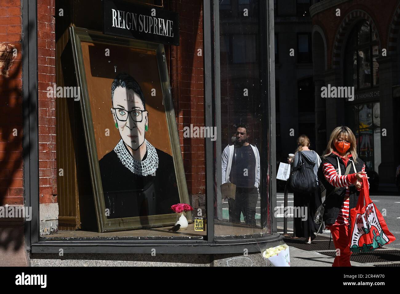 New York City, USA. September 2020. Eine Frau in einer roten Maske geht an einem Gemälde in einem Schaufenster von Ruth Bader Ginsburg, Associate Justice des Obersten Gerichtshofs der Vereinigten Staaten, vorbei, die am 18. September in New York, NY, 19. September 2020 starb. Das Porträt der Gerechtigkeit Ginsburg, das seit einem Monat im Fenster von Fishs Eddy aufgestellt wird, gemalt von der Künstlerin Julie Gaines, die auch die Eigentümerin des Ladens ist. (Anthony Behar/Sipa USA) Quelle: SIPA USA/Alamy Live News Stockfoto