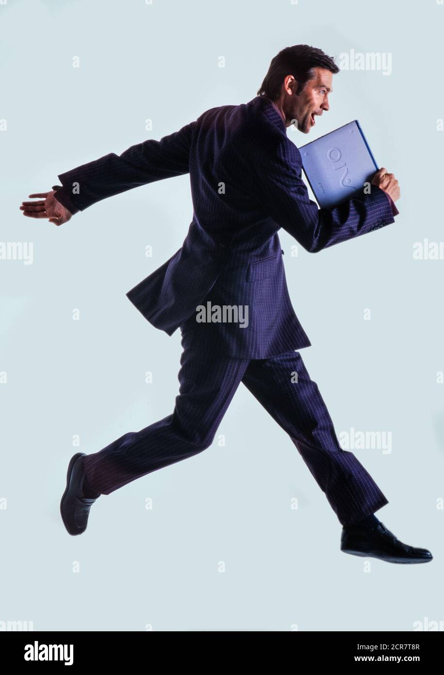 Studio Ausschnitt Porträt eines kaukasischen Geschäftsmann in Ein Anzug, der seinen Laptop umklammert und durch die Luft springt Stockfoto