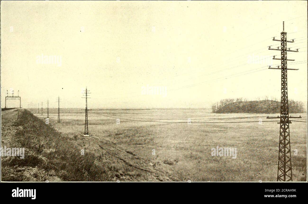 . Elektrische Eisenbahn Zeitschrift . Pennsylvania Railroad – Einstellung Transmission Line Polewith Derrick Car am Hackensack River die Stromleitung steigt scharf, inone Span, an die Spitze der hohen Türme, und erforderlich spezielle. Pennsylvania Railroad – Transmission Line Across Hackensack Meadows Dehnungsisolatoren aus zwei Teilen. Diese Isolatoren sind montierte Isolieraufsätze. Jedes Stromkabel, im Überschreiten theon gegossene Stahlstifte, die an den Stahlkanal-Querarmen verschraubt sind. Stahlkreuzarme des Turms, wird in einem Sattel getragen, der die Übertragungsleitungsmasten stützt, die die Pfannen überqueren, die durch ein Nest von getragen werden Stockfoto