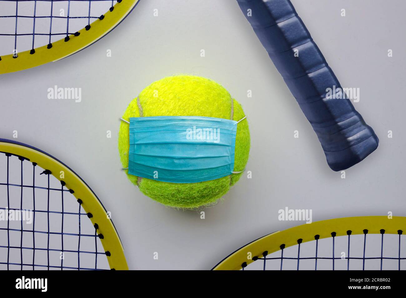 Ein Tennisball mit Gesichtsmaske und Tennisschlägern In der Nähe Stockfoto
