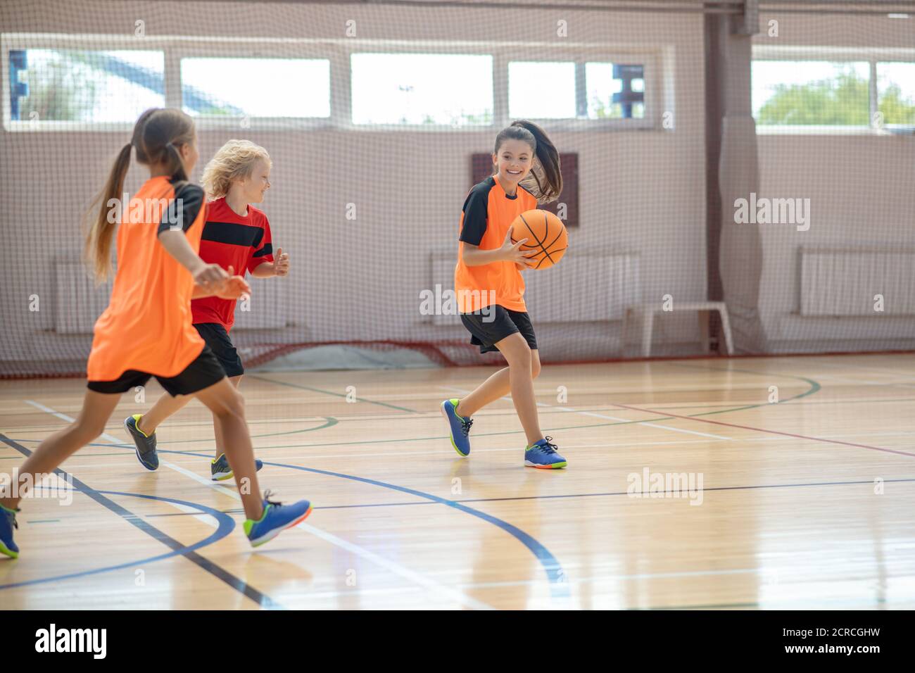 Kinder in heller Sportbekleidung spielen Basketball zusammen und laufen Stockfoto