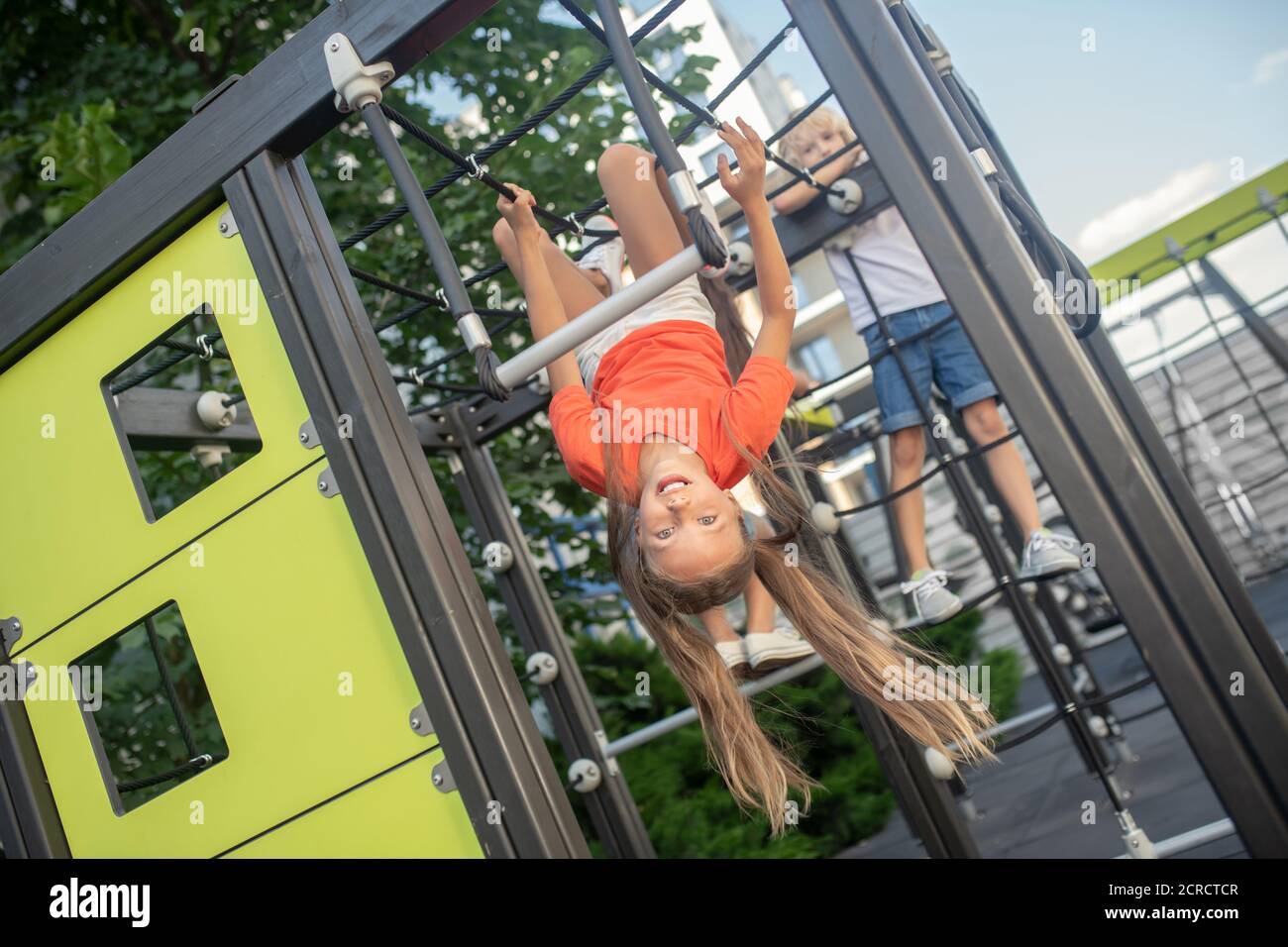 Mädchen in orange T-Shirt hängen auf einem Spielplatz im Freien Stockfoto