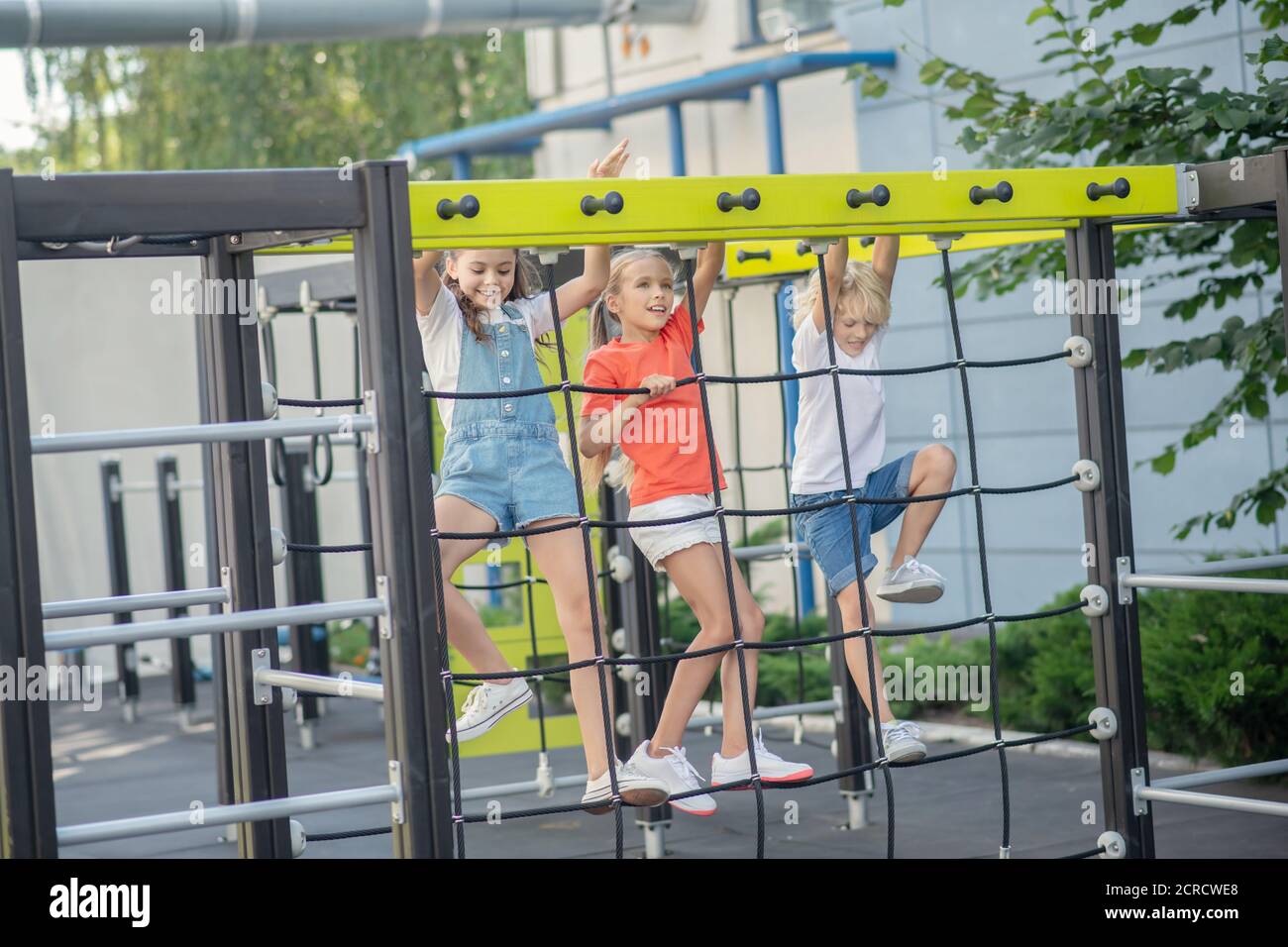 Drei Kinder klettern auf Spielplatz im Freien und freuen sich Stockfoto