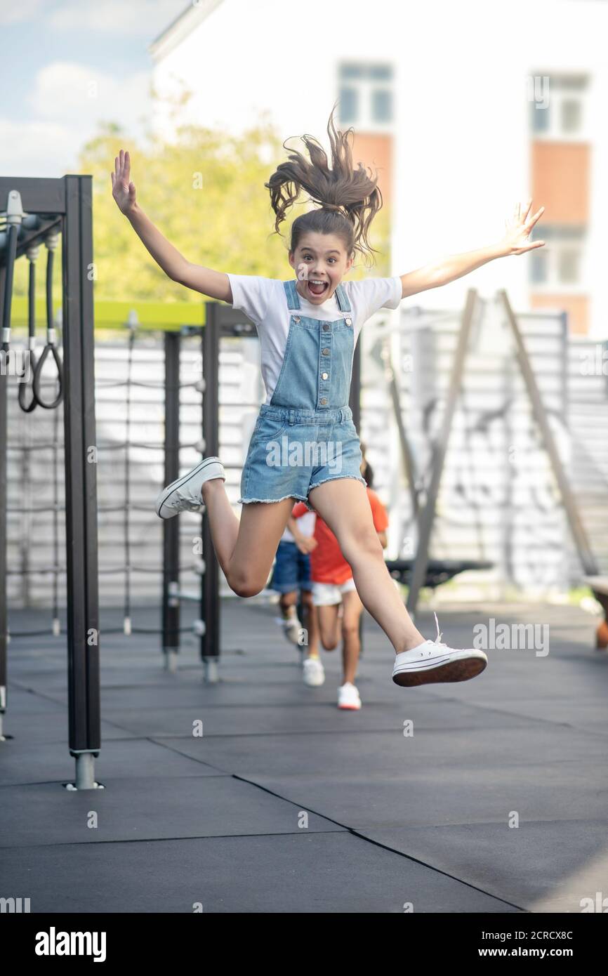 Nettes Mädchen in Denim springen beim Spielen mit Freunden Stockfoto