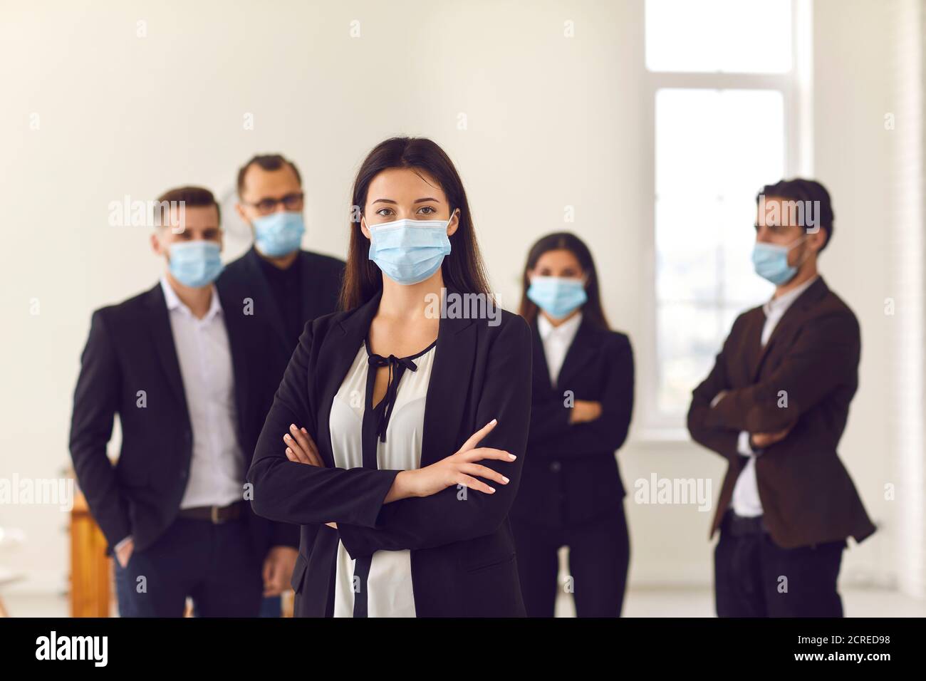 Business Frau in medizinischen Schutzmaske im Büro mit stehen Kollegen im Hintergrund Stockfoto
