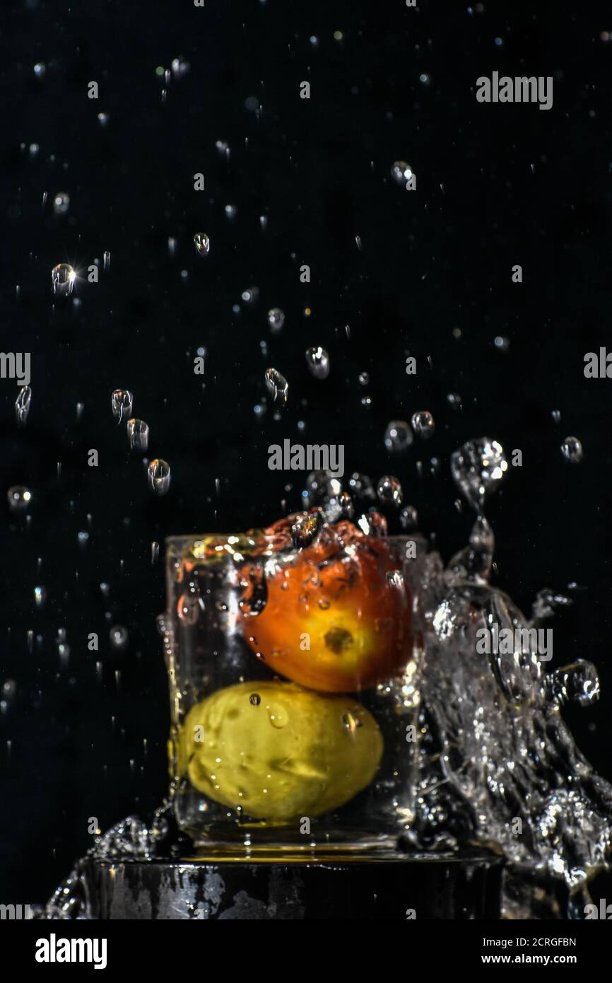 Spritzer rote Tomaten und gelbe Zitrone tauchen in Glas Von Wasser mit schwarzem Hintergrund Stockfoto