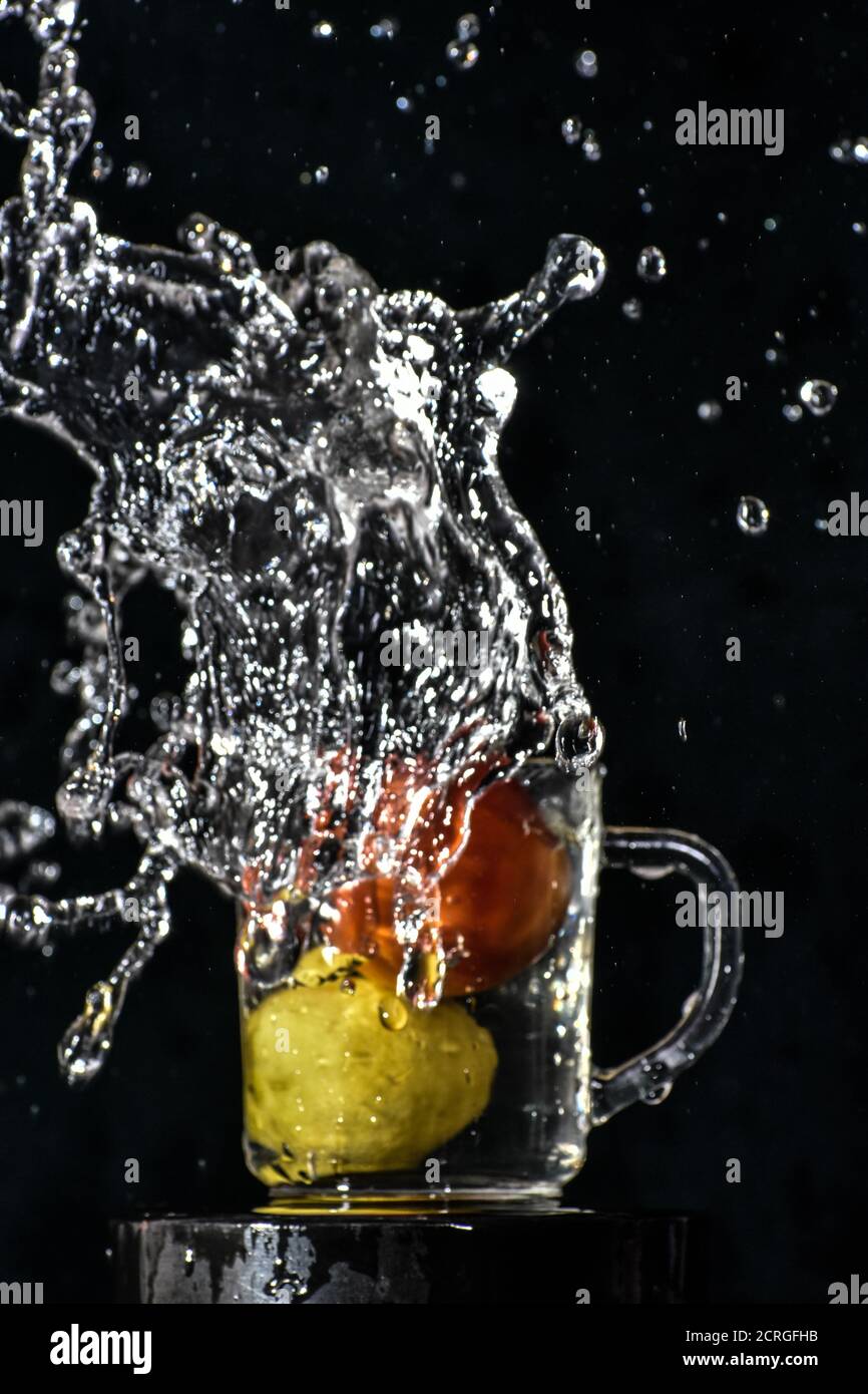 Spritzer rote Tomaten und gelbe Zitrone tauchen in Glas Von Wasser mit schwarzem Hintergrund Stockfoto