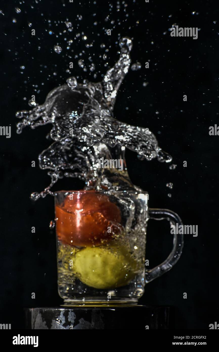 Spritzer rote Tomaten und gelbe Zitrone tauchen in Glas Von Wasser mit schwarzem Hintergrund Stockfoto
